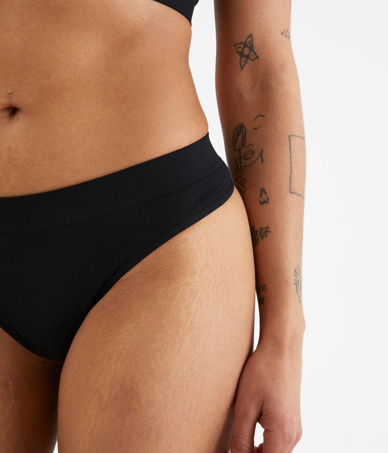 Lähikuva naisesta mustissa saumattomissa string-alushousuissa ja mustissa rintaliiveissä.