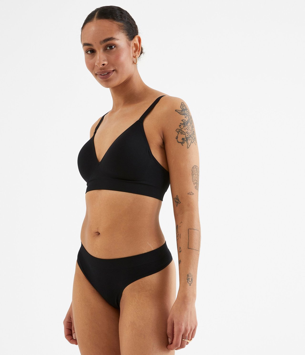 Sidebilde av en kvinne som har på seg en svart sømløs stringtruse og en matchende svart sømløs BH.