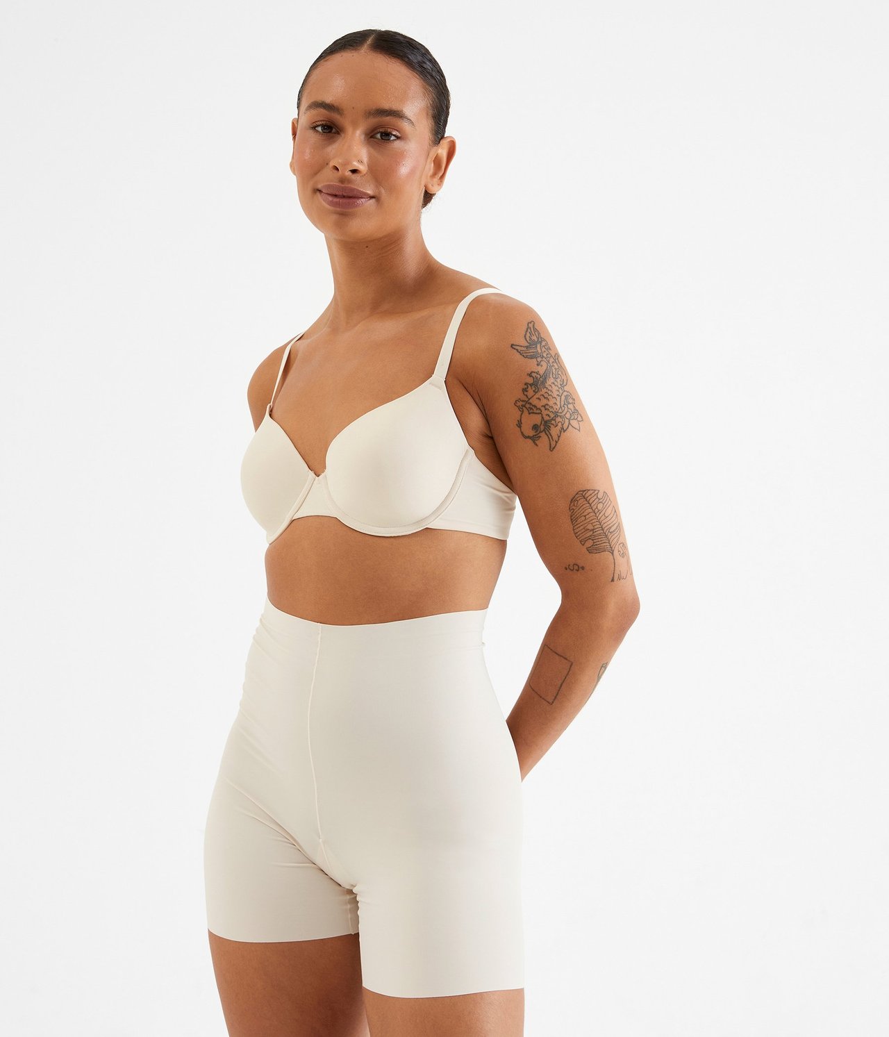 Framifrån: Kvinna i beige vadderad bygel-bh och matchande högmidjade shorts.