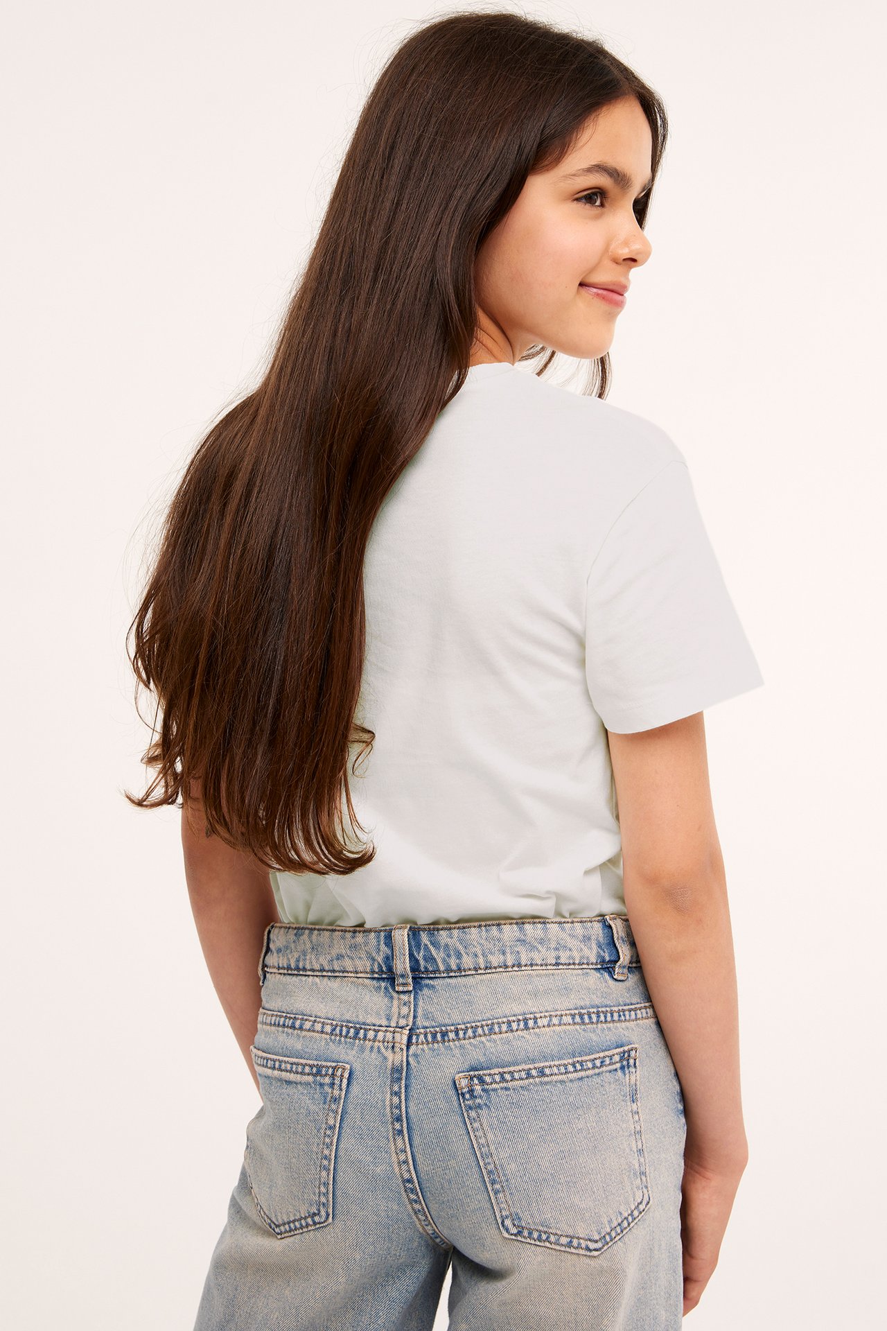 Bakifrån, ett barn i en offwhite kortärmad bomulls-t-shirt och ljusblå jeans.