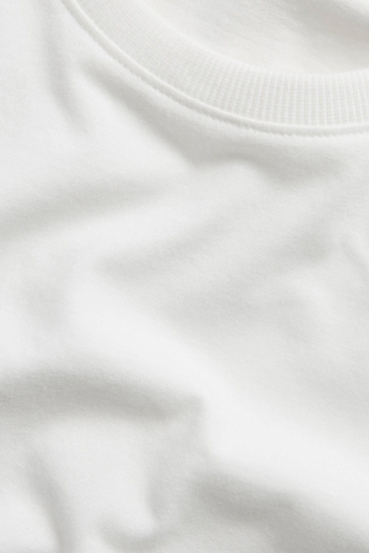 Nærbilde av en offwhite ensfarget bomulls-T-skjorte med ribbet rund hals.