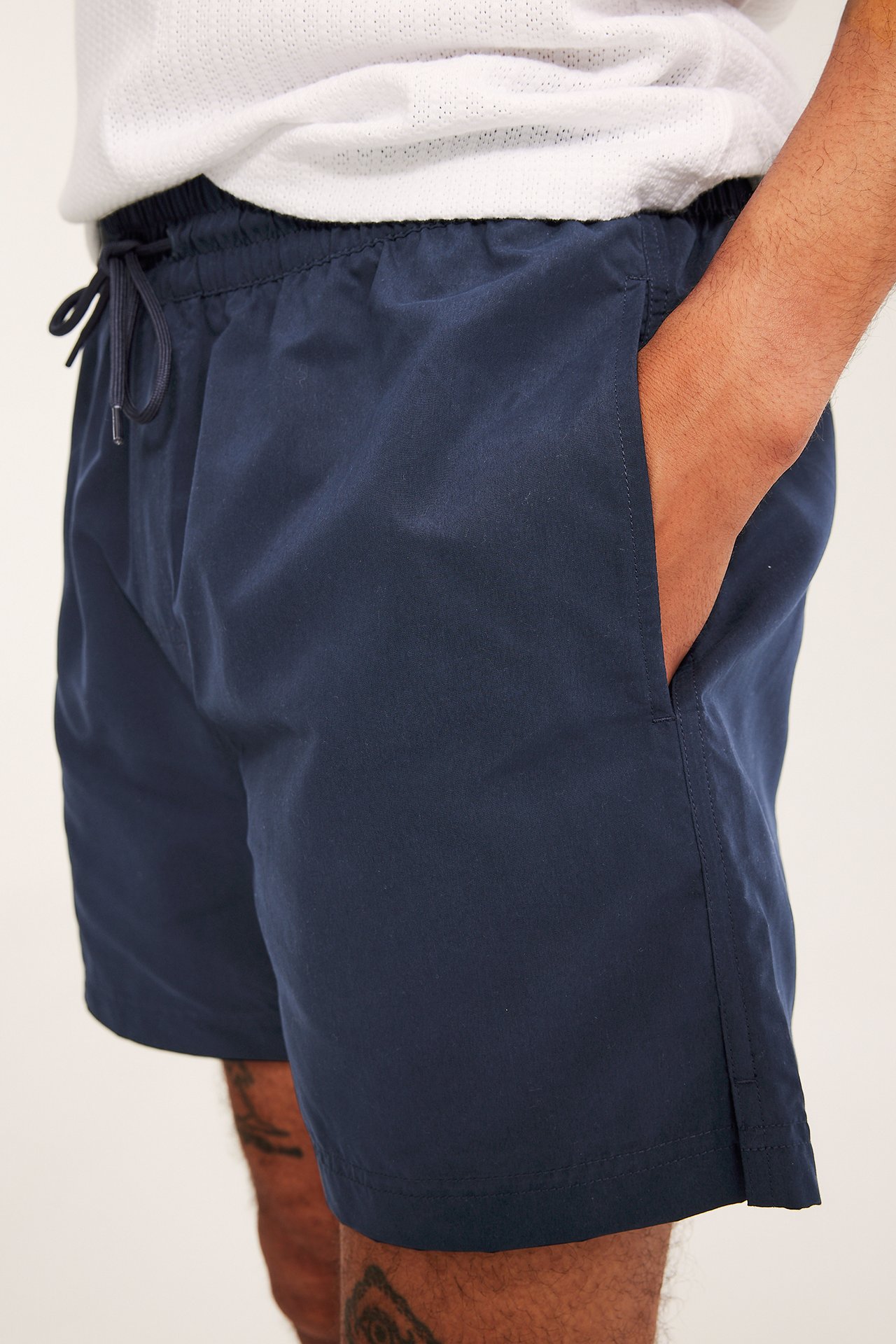 Sidebilde av en mann i mørkeblå badeshorts av resirkulert polyester med strikk i livet, snøring, sidelomme.
