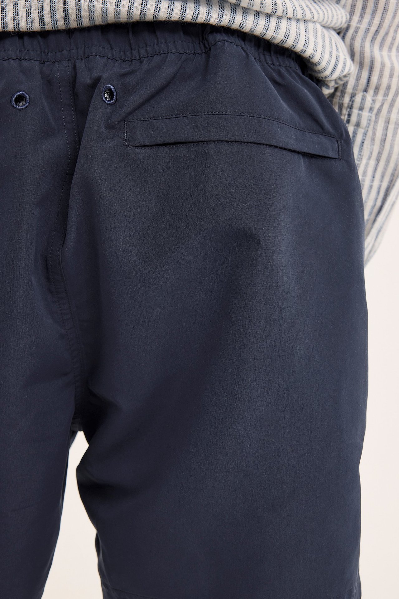 Lähikuva miehen tummansinisistä uimashortseista, joissa on joustava vyötärö ja läpällinen takatasku.