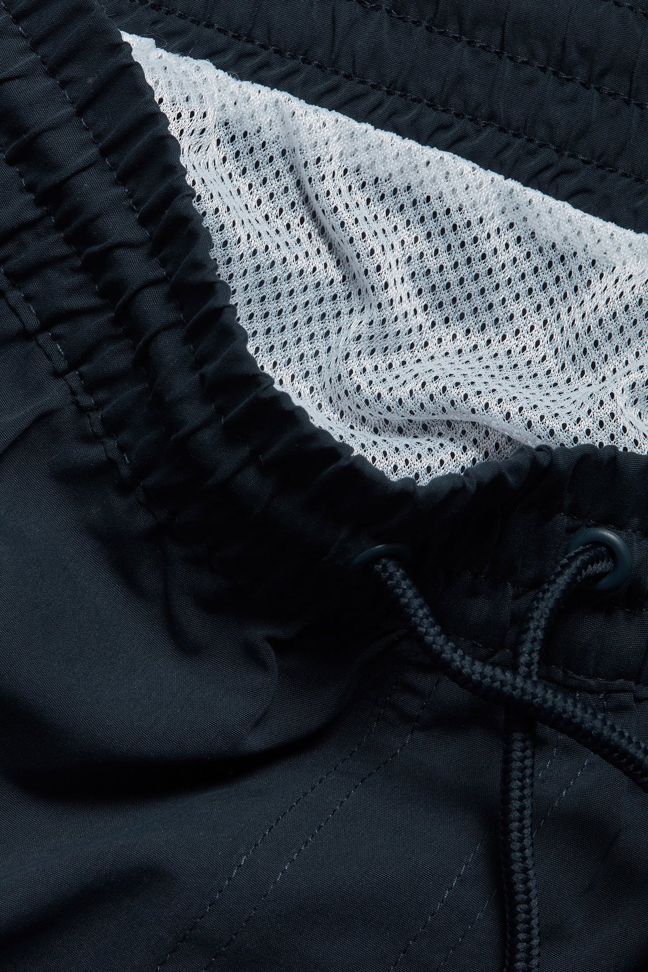 Zbliżenie: Męskie ciemnoniebieskie szorty kąpielowe, elastyczny pas ze sznurkiem, biała siateczka.