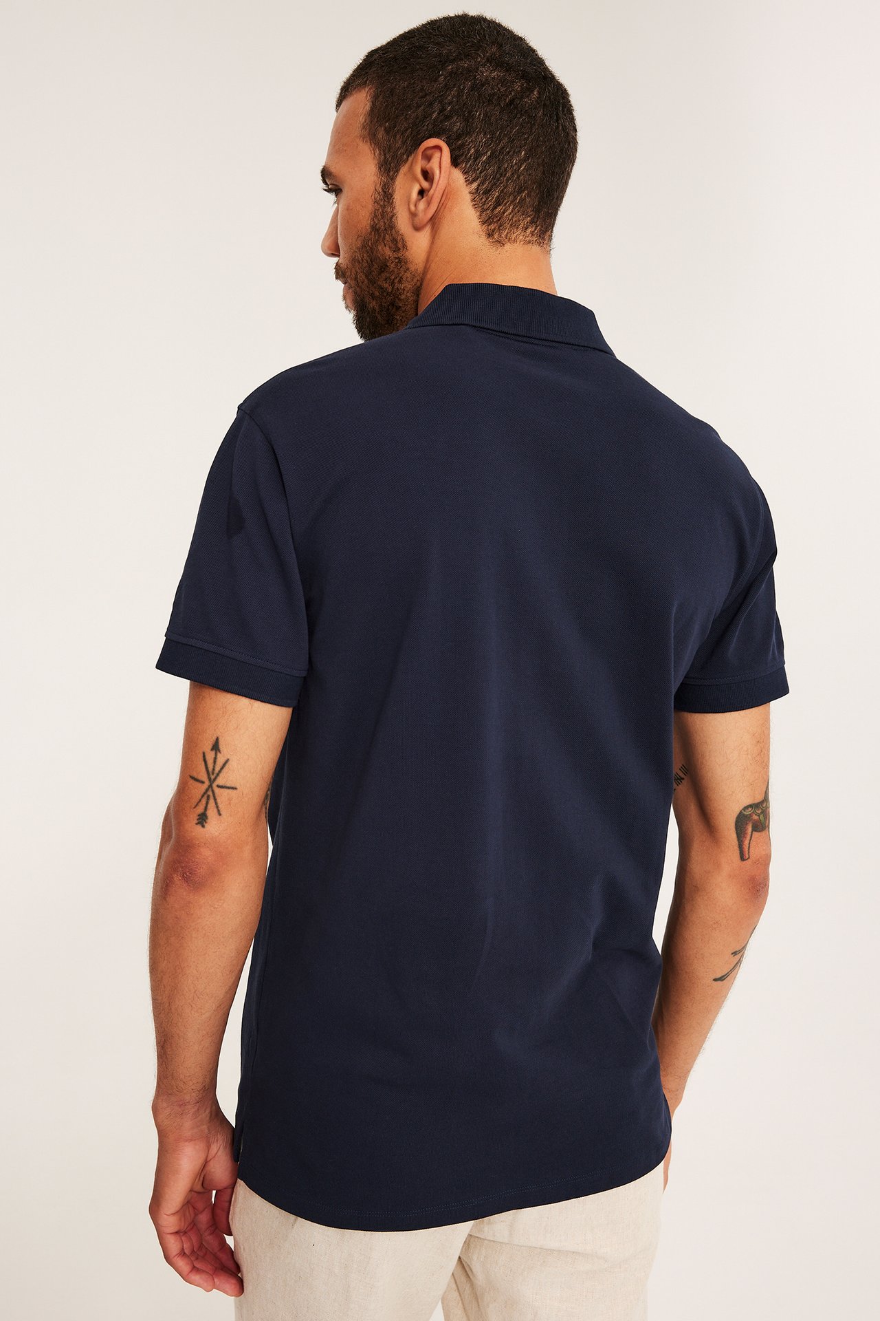 Ryggbilde av en mann i en mørkeblå kortermet bomulls-piké og lysebeige bukser.