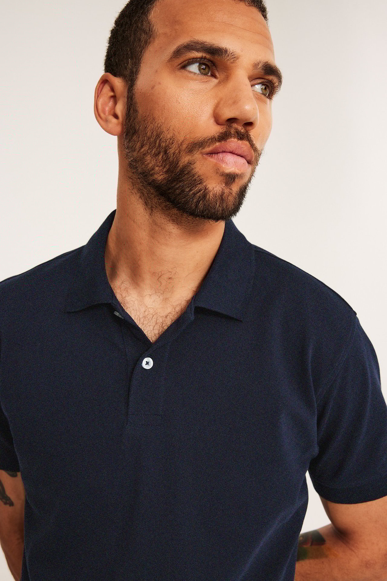 Nærbilde, forfra av en mann i mørkeblå, kortermet bomulls-pikétrøye med to hvite knapper.