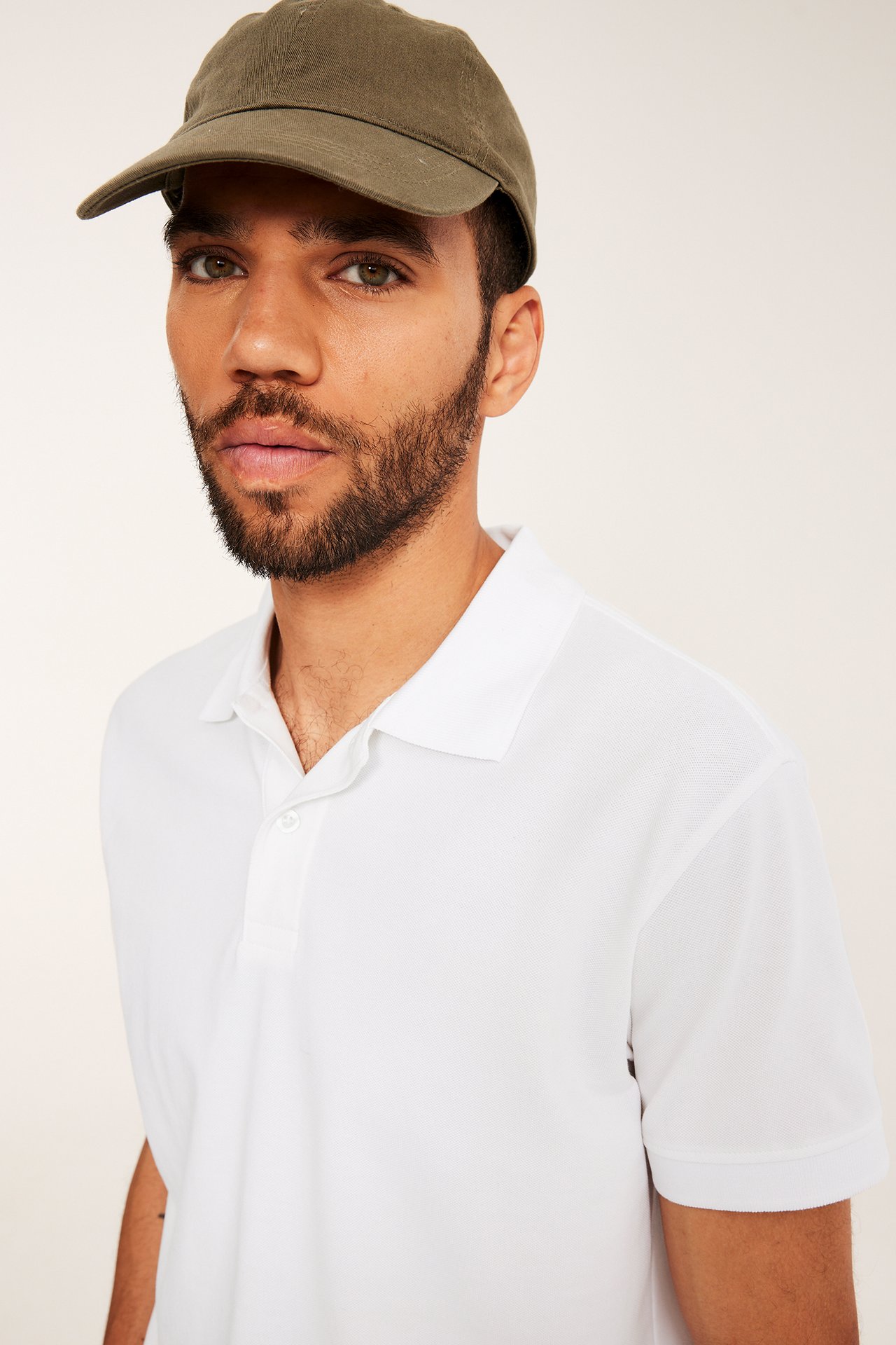Frontalvisning: Mann i hvit kortermet bomullspikéskjorte med to knapper og olivengrønn caps.