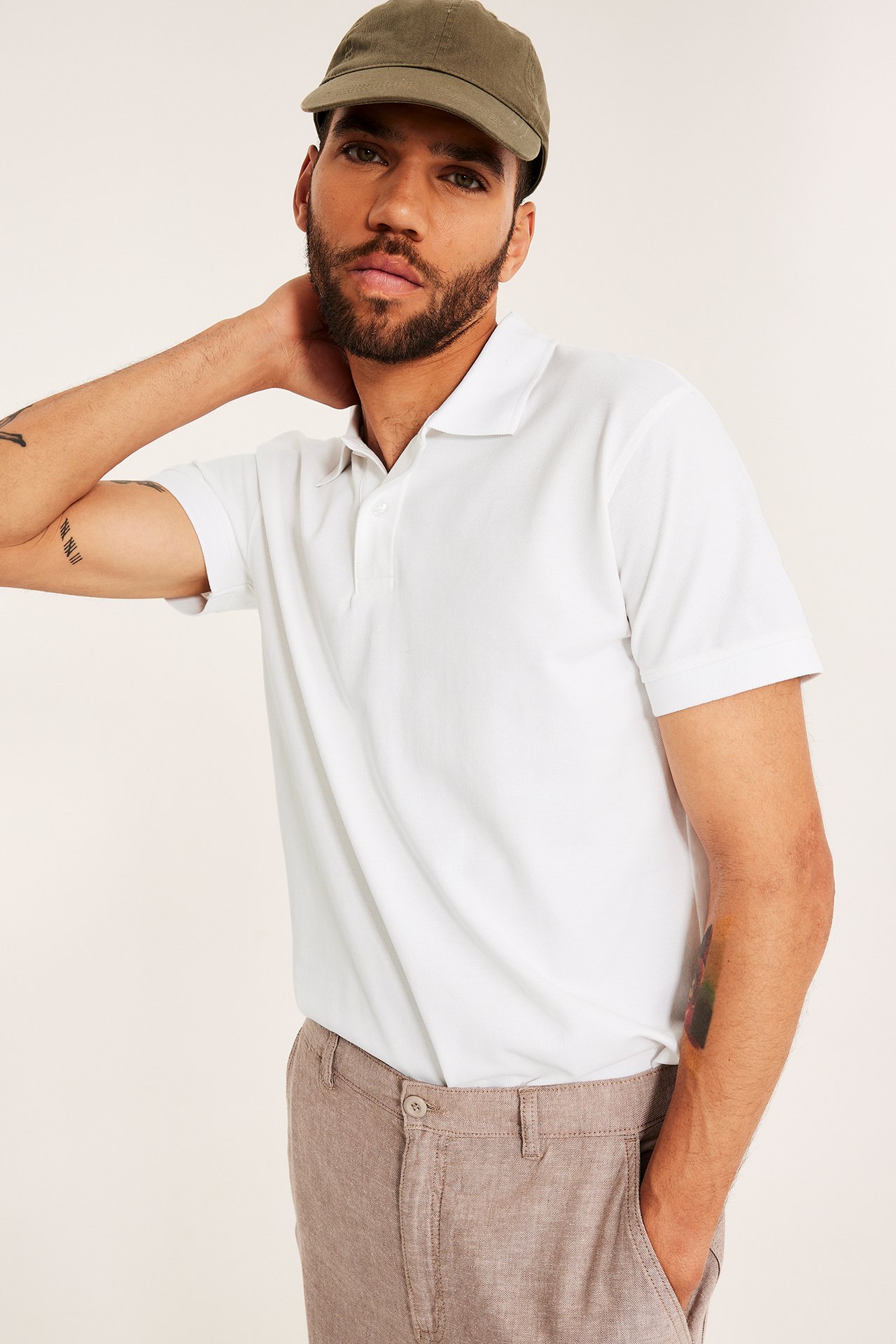 Forfra: mann i hvit toknapps pikétrøye, lysebrune bukser og olivenfarget caps.