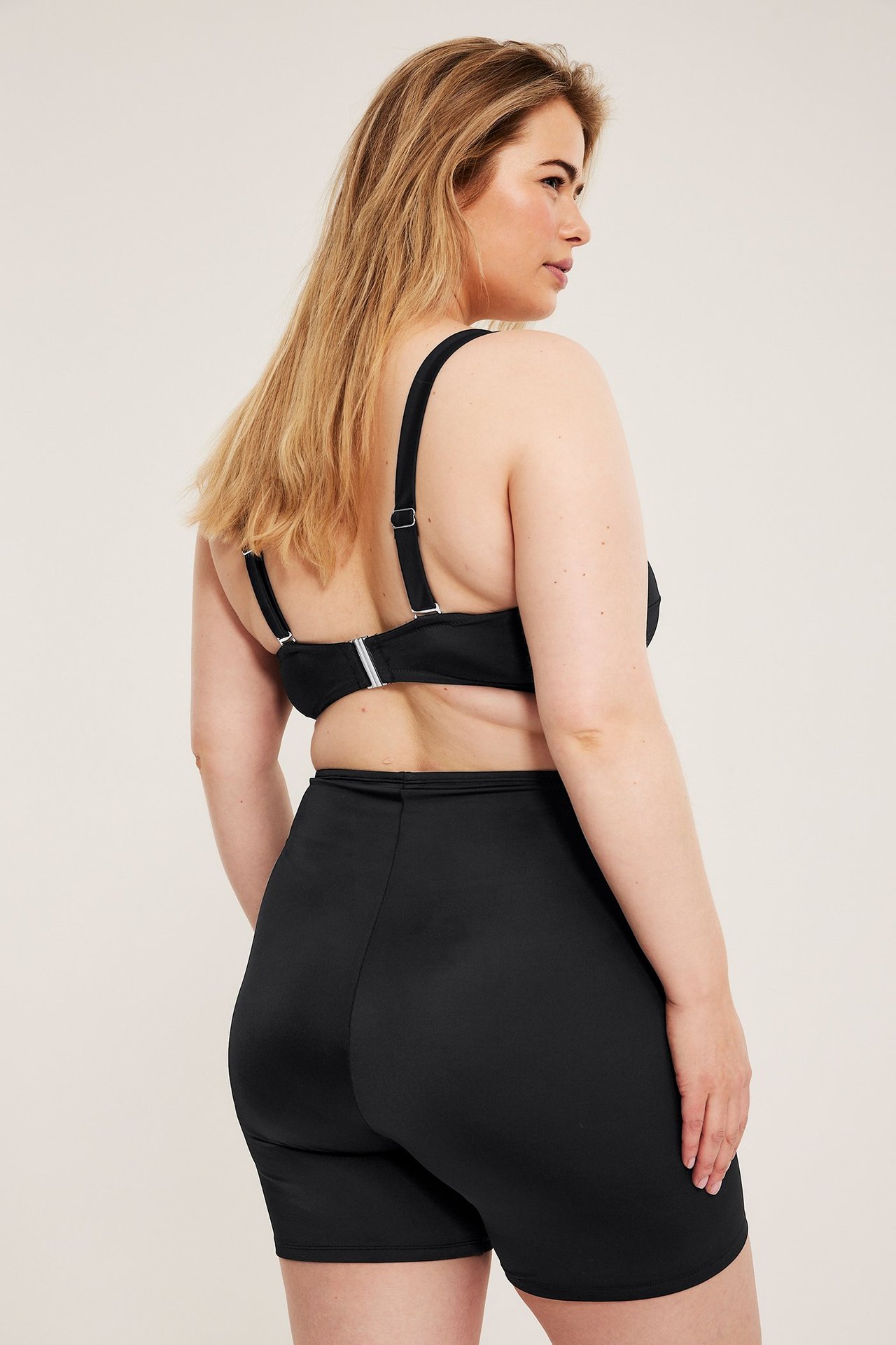 Kvinne bakfra i svarte høywaist badeshorts og en svart bikinitopp.