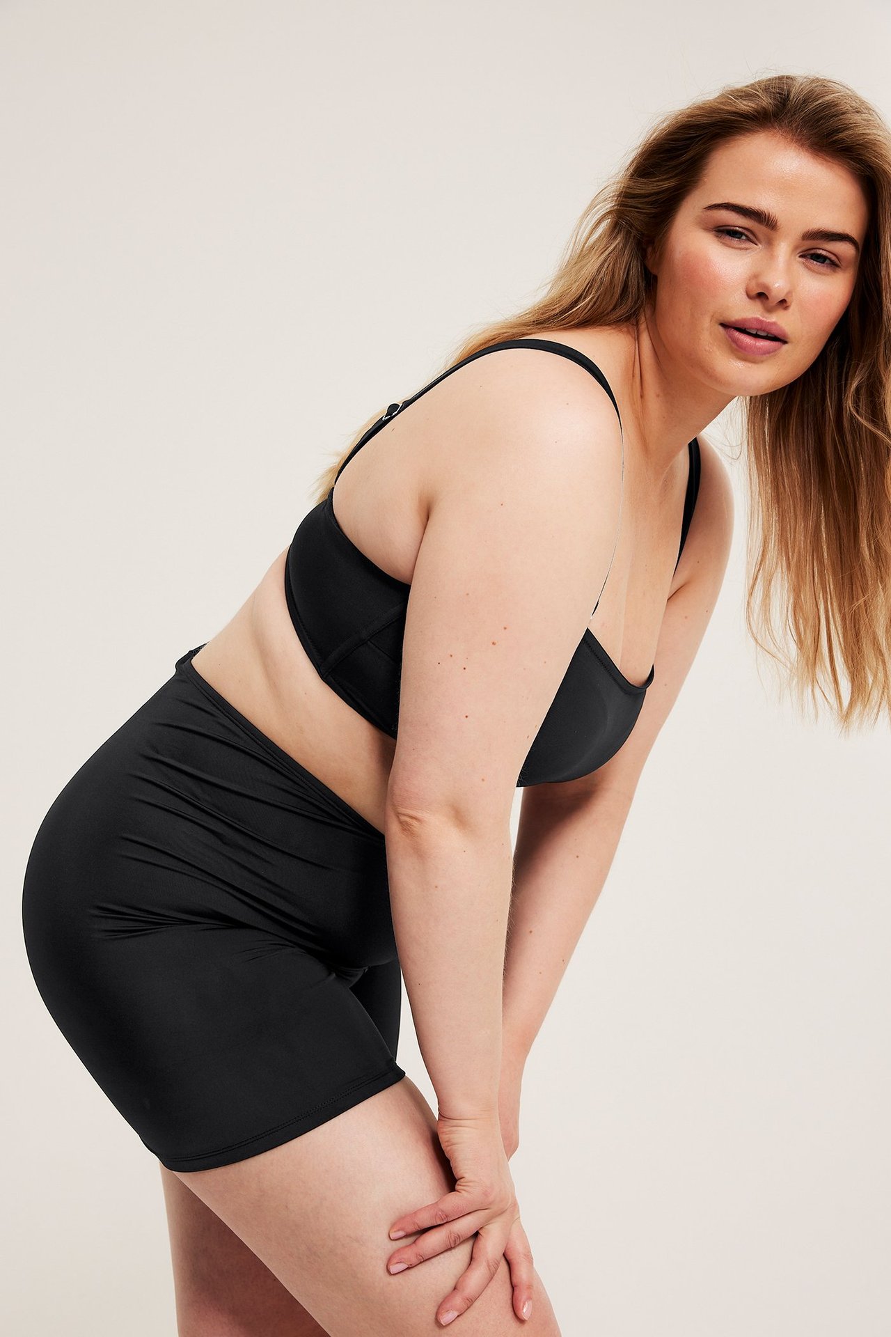 Widok z boku kobiety w czarnych szortach kąpielowych z wysokim stanem i pasującym czarnym biustonoszu bikini.