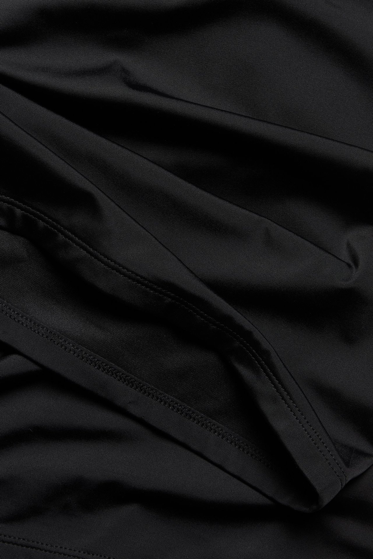 Zbliżenie na czarne, jednolite szorty kąpielowe z wysokim stanem, z widocznymi szwami i fałdami materiału.