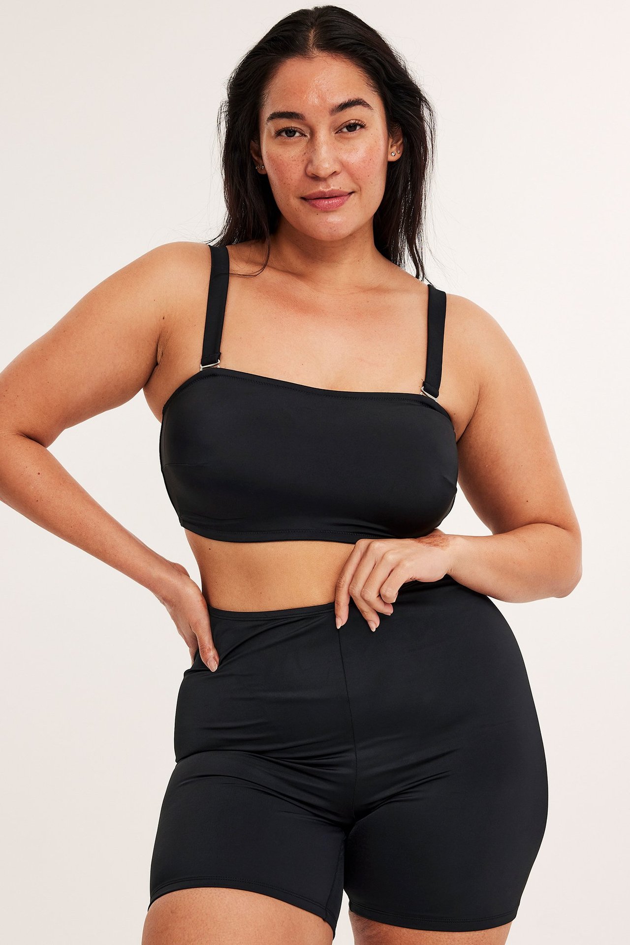 Widok z przodu kobiety w czarnych szortach kąpielowych z wysokim stanem i pasującym czarnym topie bandeau.