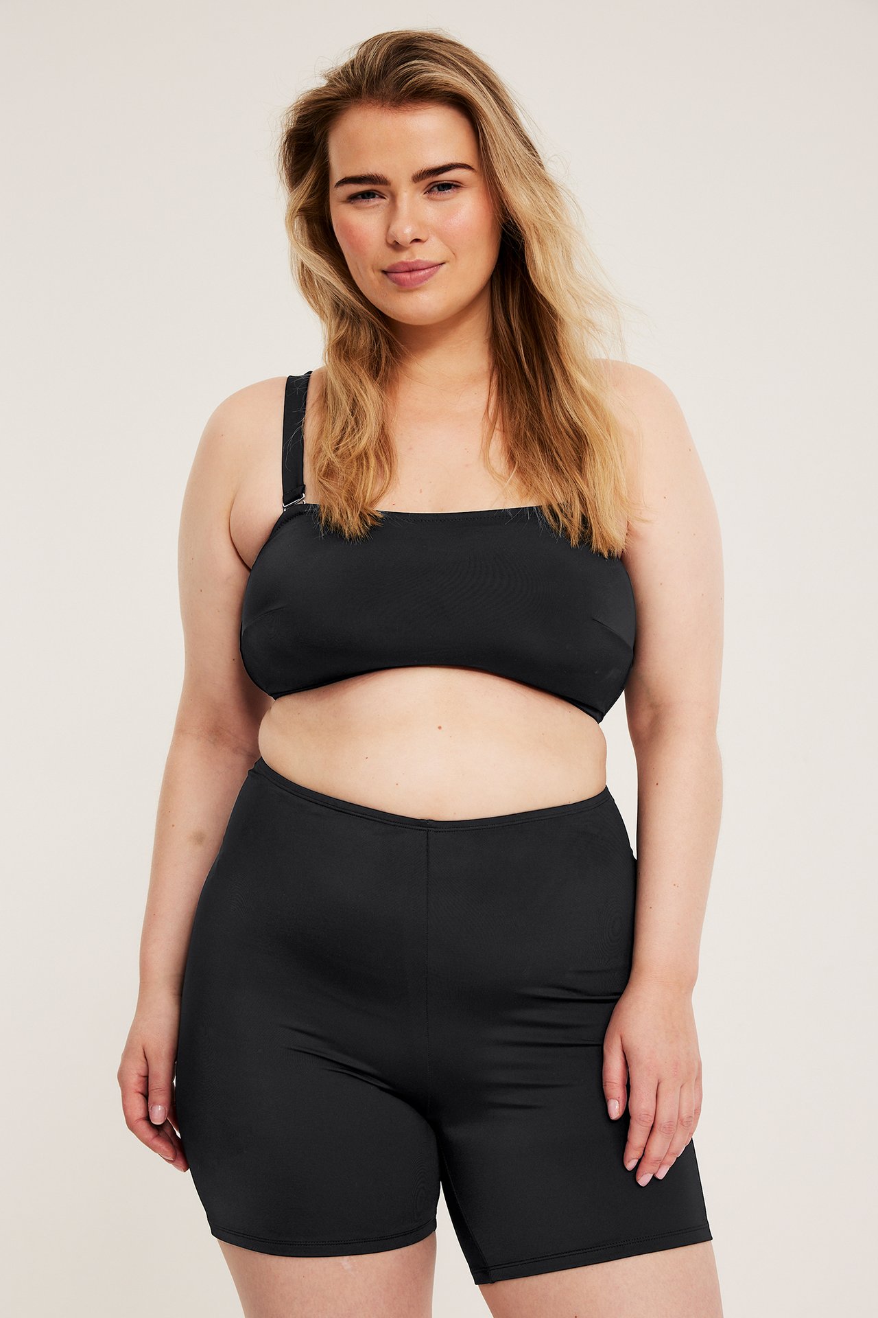 Forfra: kvinne i svarte, høy midje bikeshorts og en svart bikinitopp med firkantet hals.