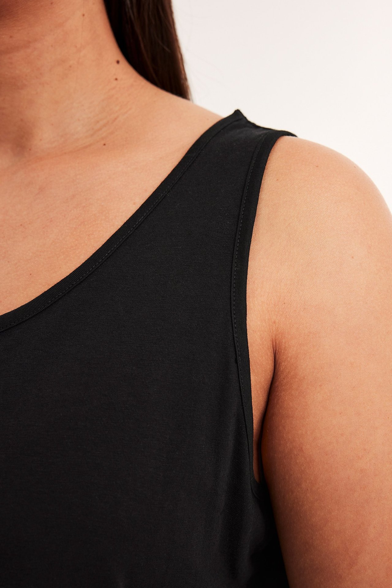Nærbilde av en kvinne i en svart jersey-tanktopp, som viser halslinje og skulder.