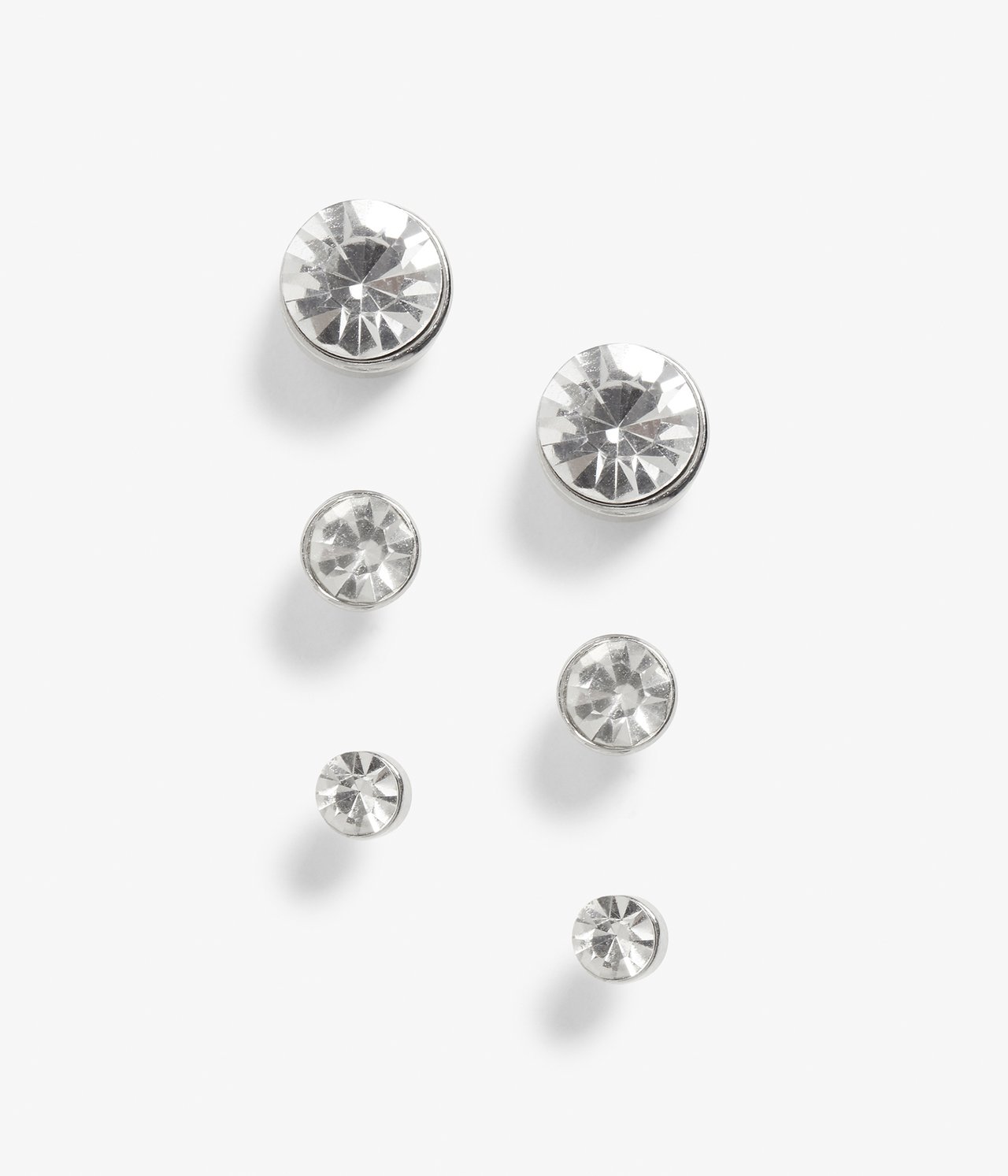 Närbild av ett 3-pack silverfärgade stiftörhängen med klara stenar i olika storlekar.