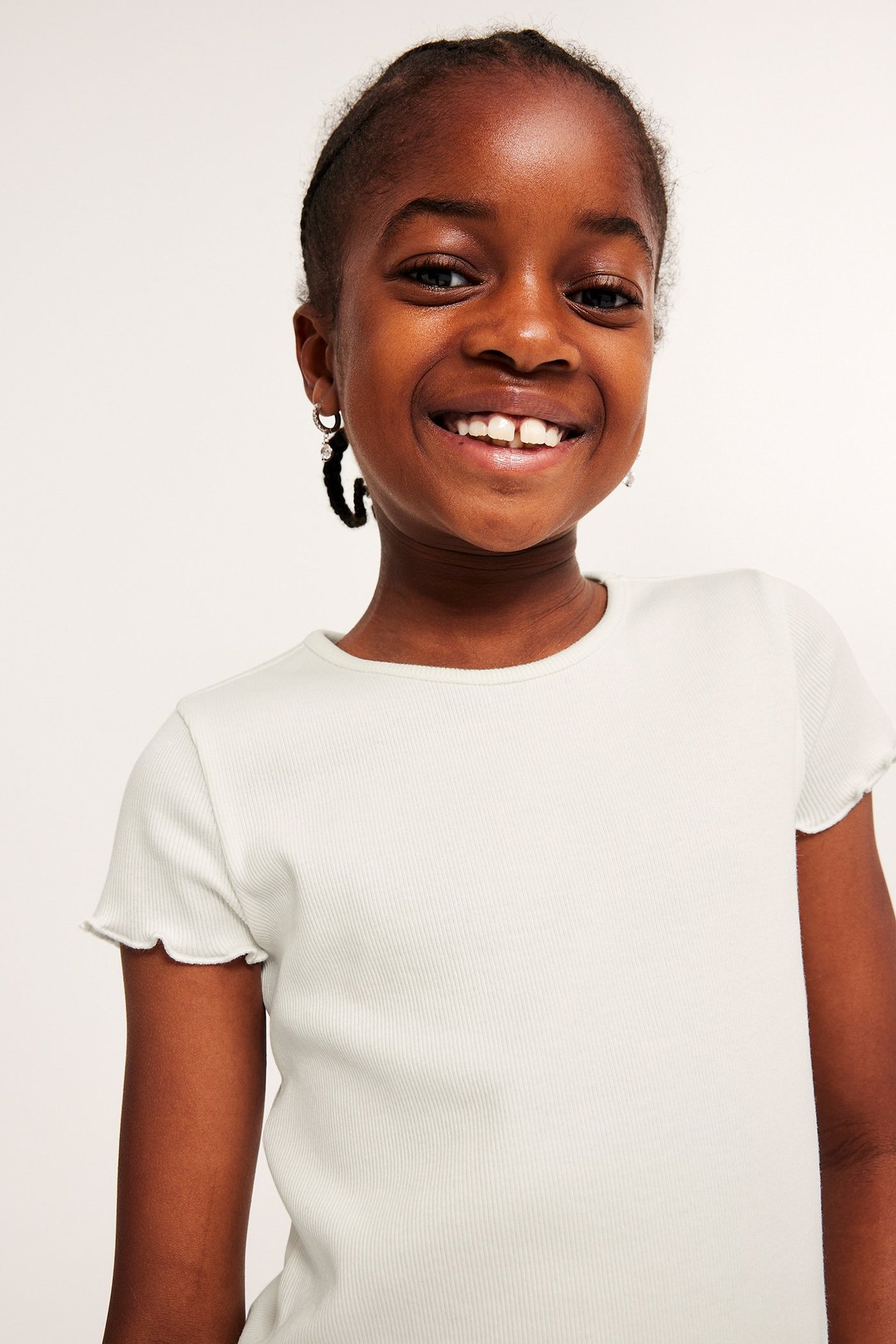 Framsida av ett barn som bär en offwhite kortärmad ribbad topp med babylock-kanter.