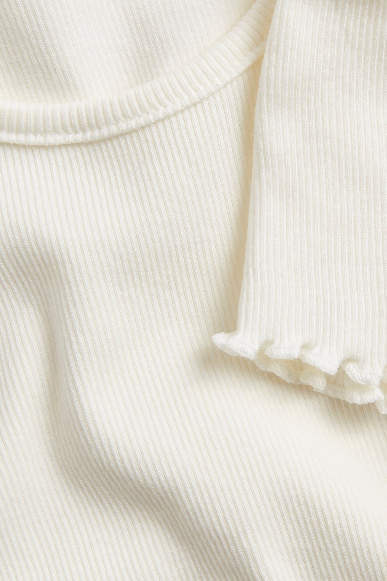 Zbliżenie na kremowy, prążkowany top z krótkim rękawem i wykończeniem babylock na rękawie.