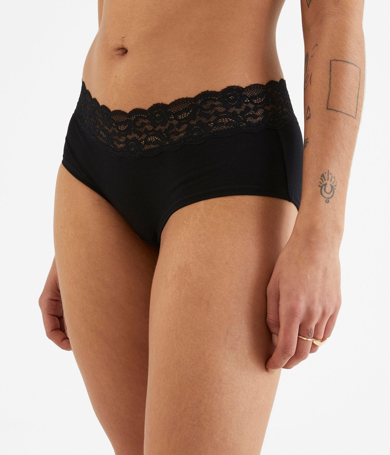 Widok z przodu kobiety w czarnych bawełnianych figach typu hipster z koronkowym pasem i złotym pierścionkiem.