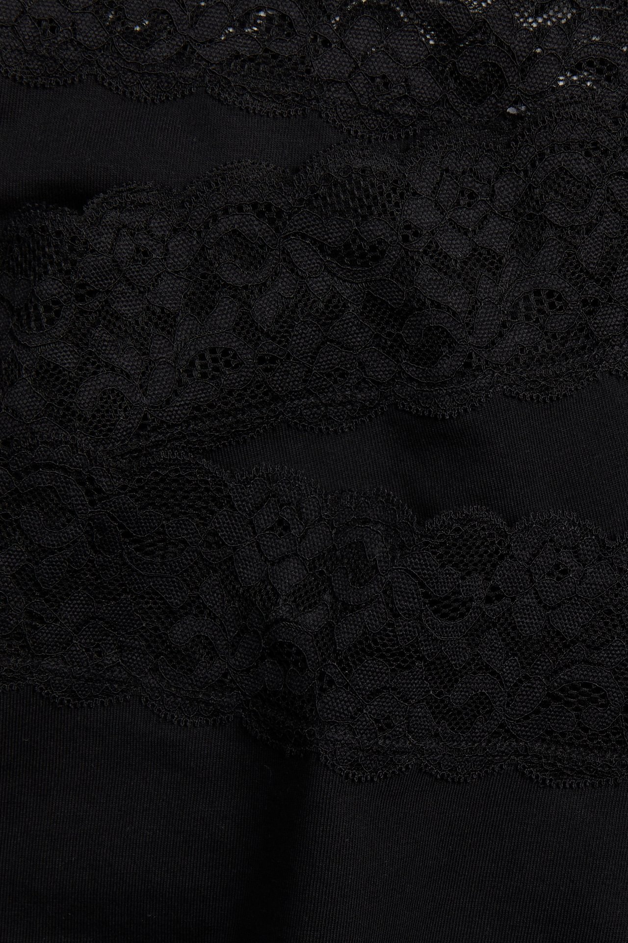 Närbild på svarta bomullshipstertrosor med breda band av svart blommönstrad spets.