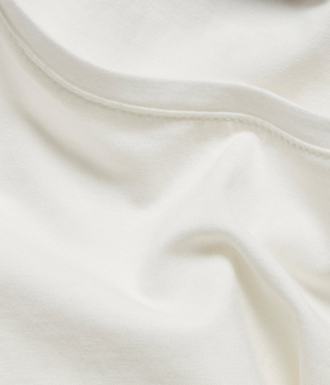 Zbliżenie na kremowy, długi rękaw, podstawowy top, pokazujące miękki materiał i szew dekoltu.