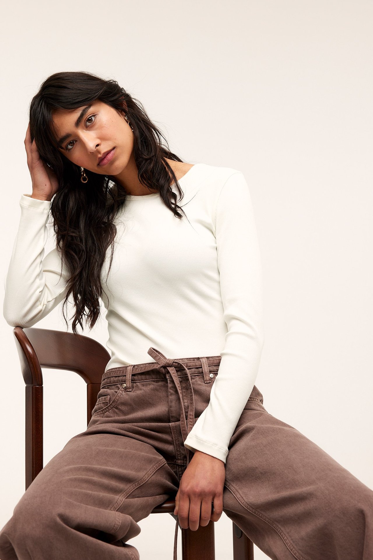 Forfra: kvinne i offwhite ribbet langermet topp og brune vide bukser med snøring.