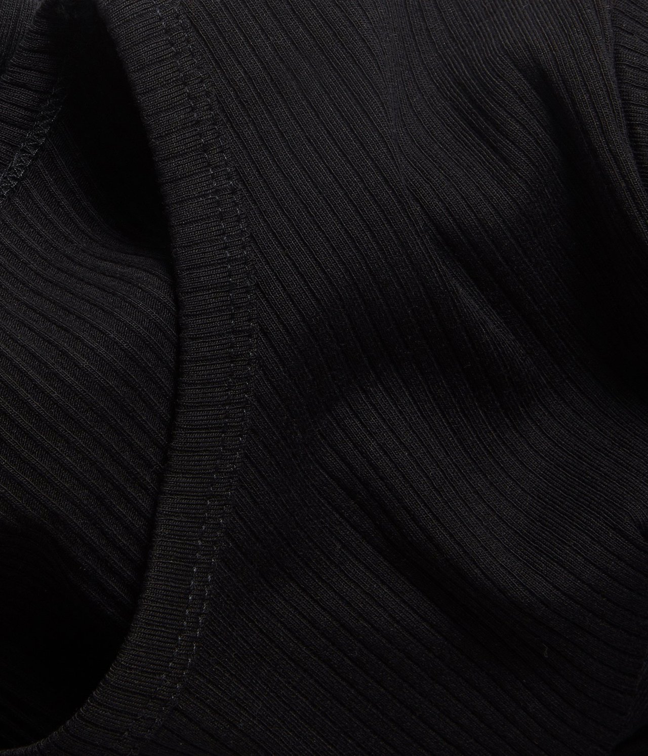 Nærbilde av svart ribbet stoff fra en topp, som viser teksturen og en søm.