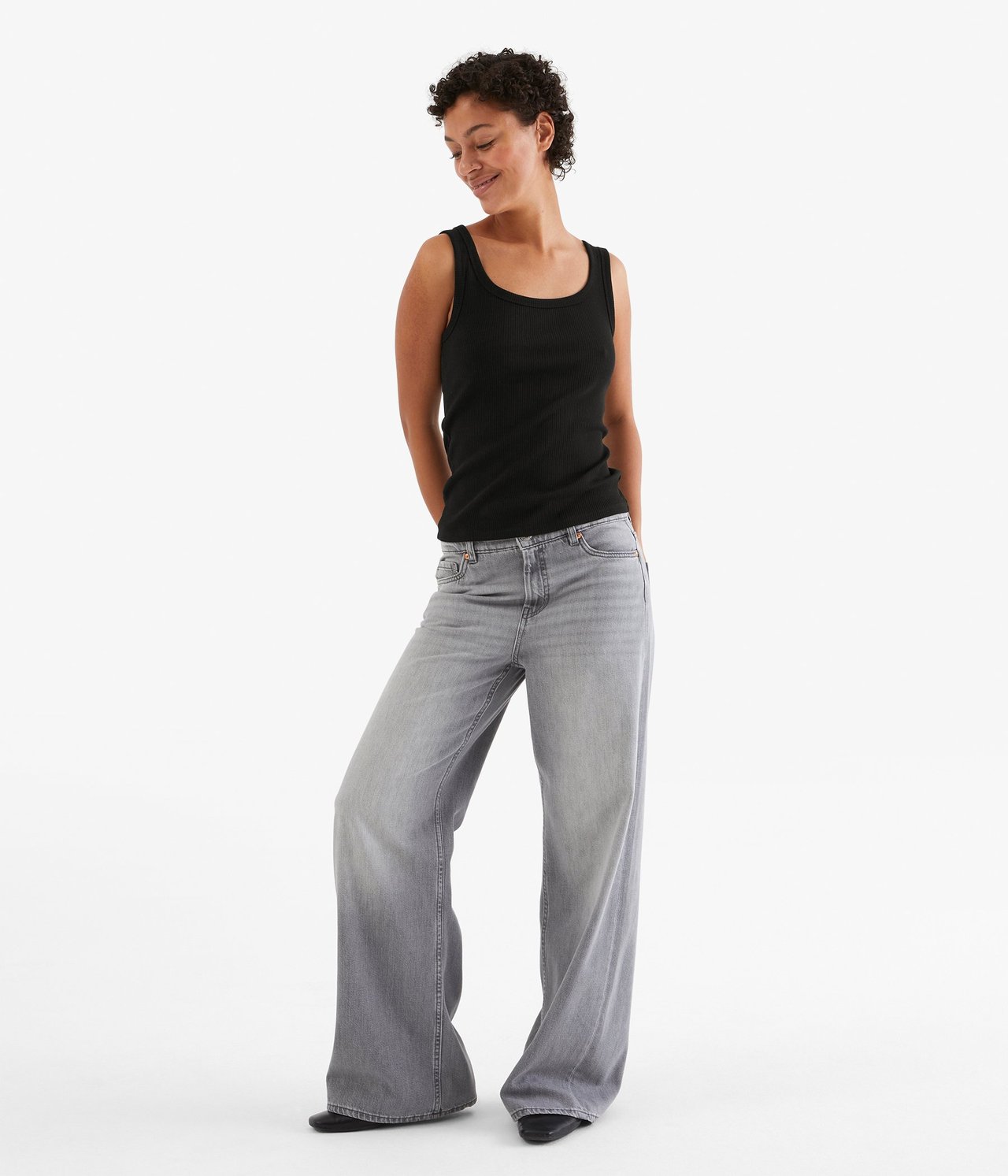 Forfra: Kvinne i svart ribbet singlet og grå vide jeans.