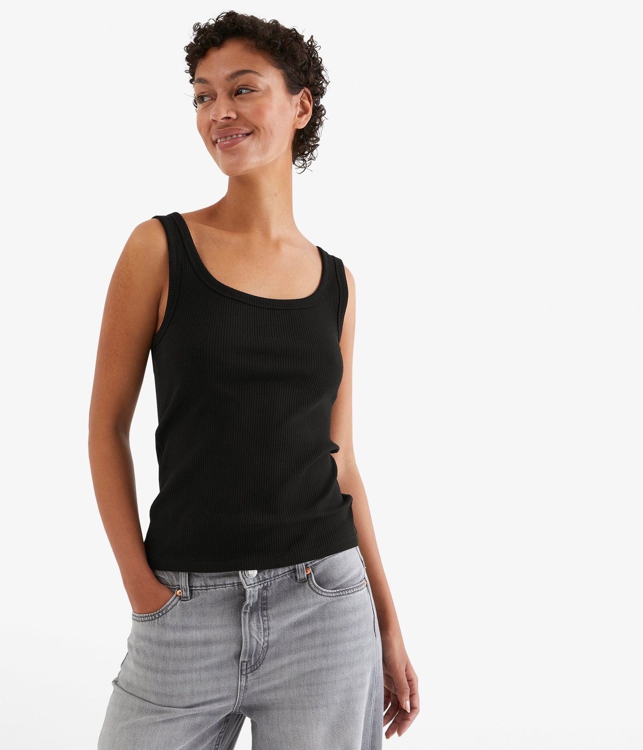 Frontvisning av en kvinne i en svart ribbet singlet og lysegrå jeans.