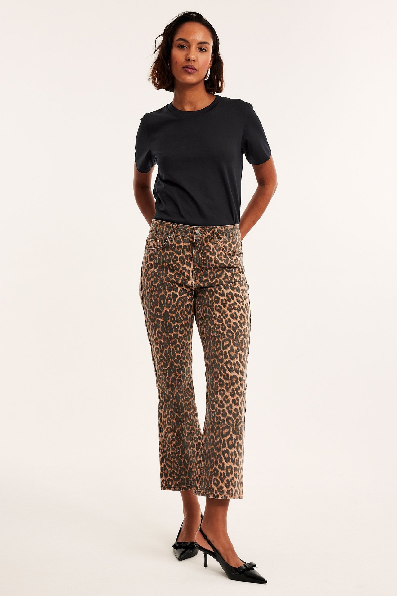 Forfra: kvinne i svart bomulls-T-skjorte, leopardmønstrede cropped jeans og svarte slingback-hæler.