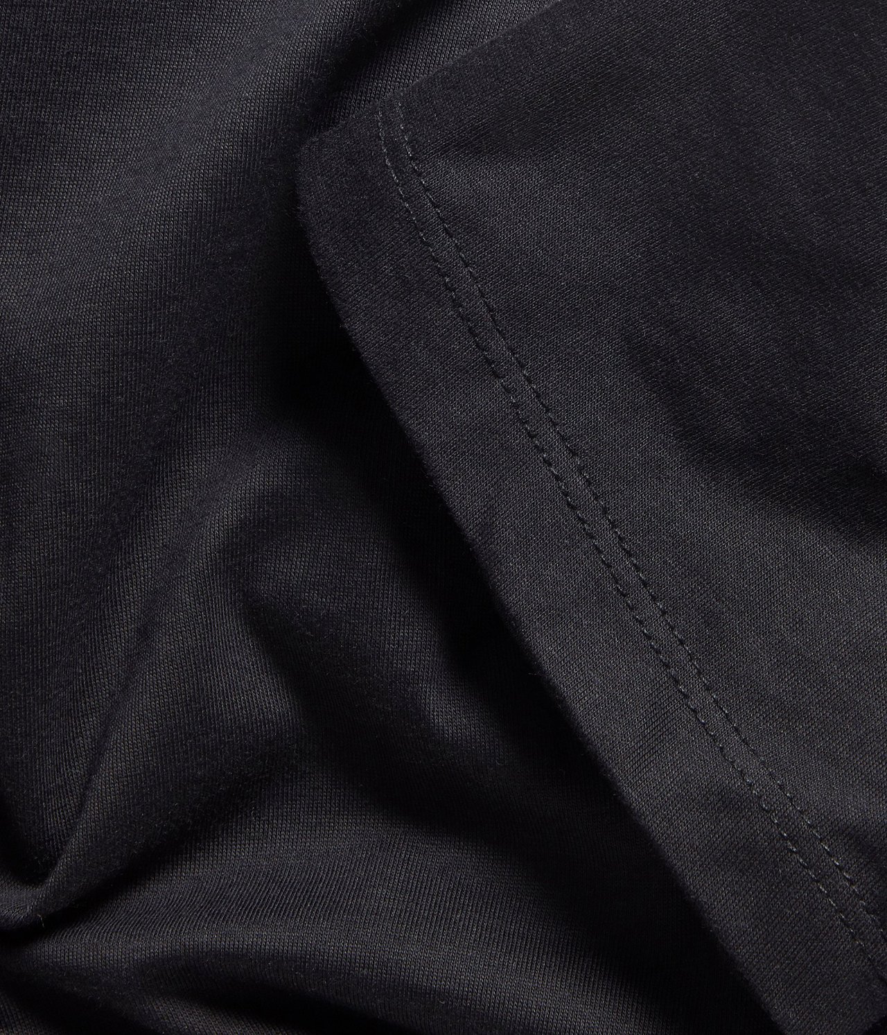 Zbliżenie czarnego materiału bawełnianej koszulki, ukazujące szew i subtelną teksturę.