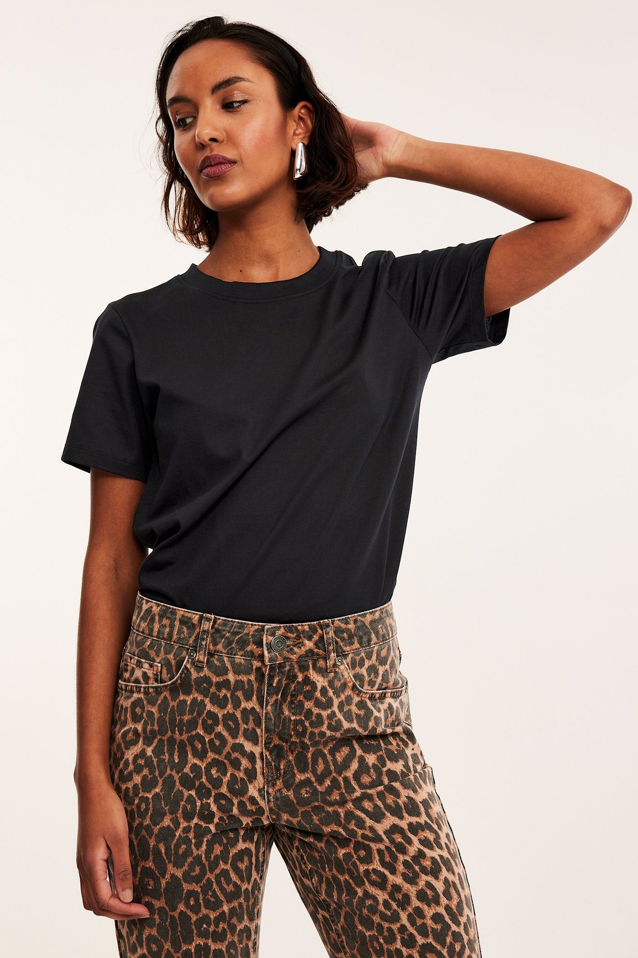 Forfra: kvinne i svart bomulls-T-skjorte, leopardmønstrede jeans og sølvfargede øreringer.