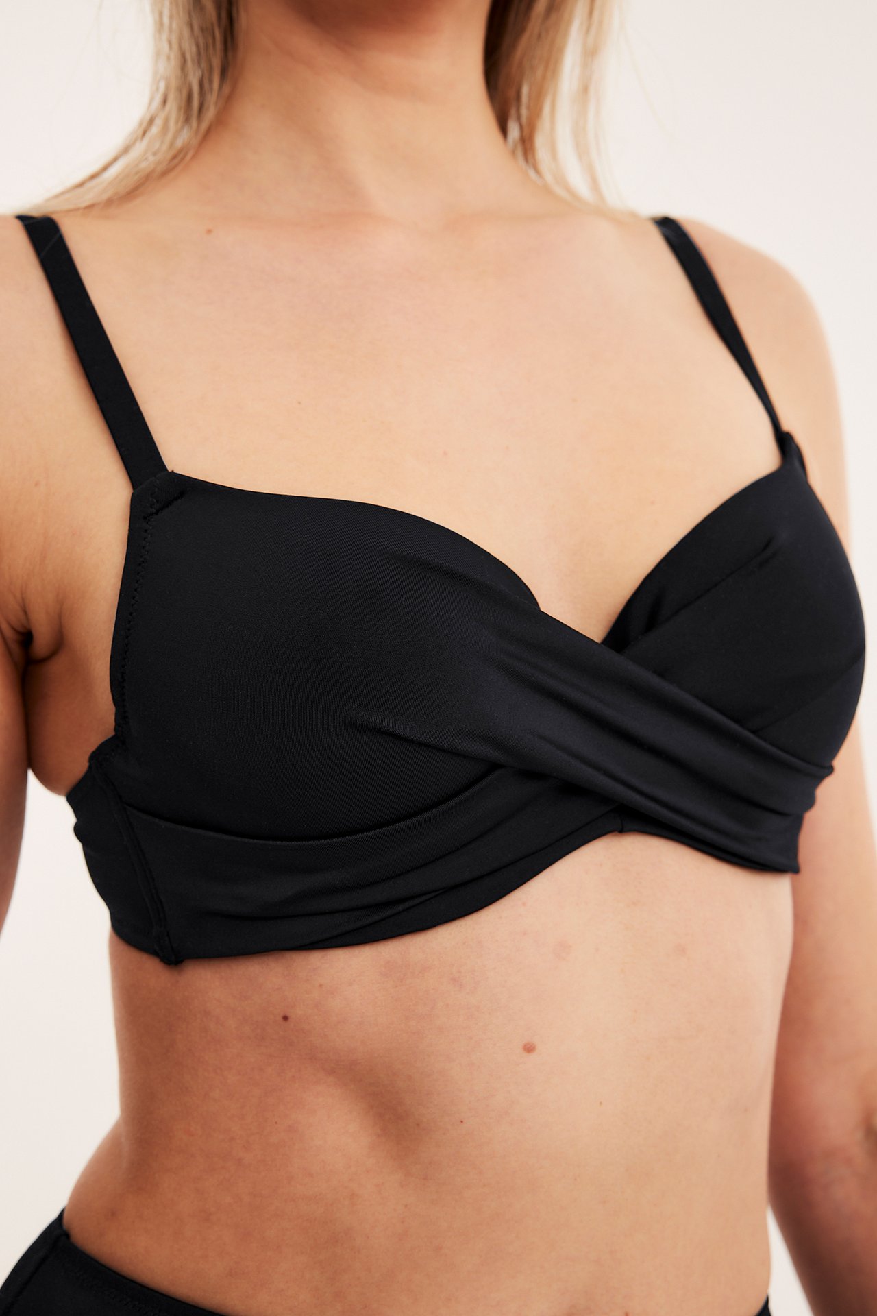 Nærbilde forfra av en kvinne i svart ensfarget bikini-BH med vridd detalj og justerbare skulderstropper.