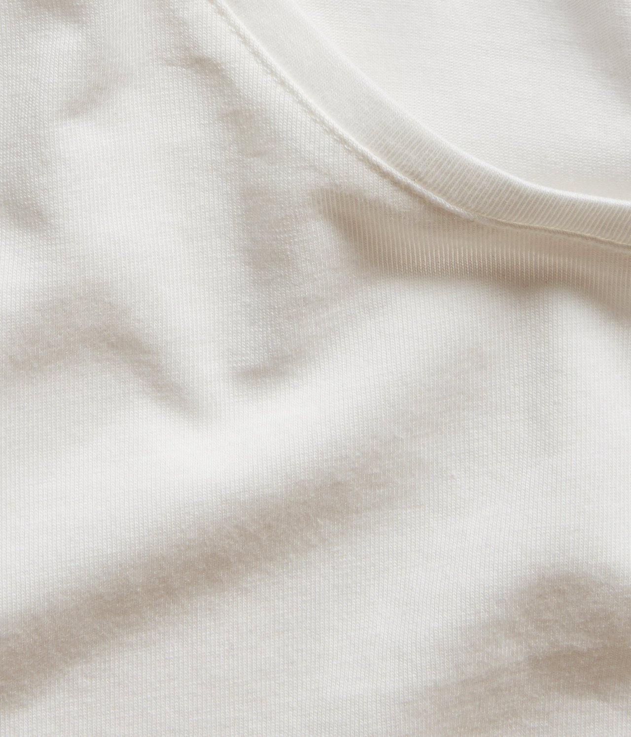 Nærbilde av en offwhite kortermet basetopp med rund hals, som viser bomullsblandingsstoffet.