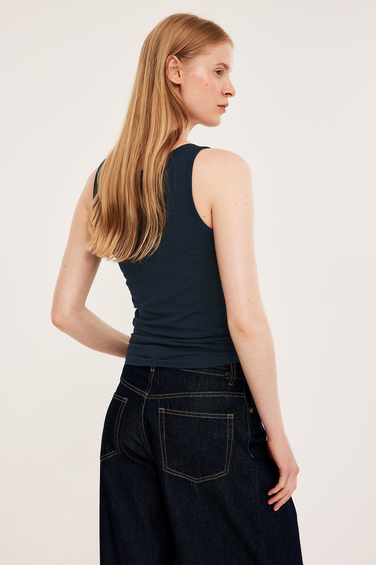 Bakifrån: kvinna i mörkblått åtsittande bomullslinne och mörka jeans.