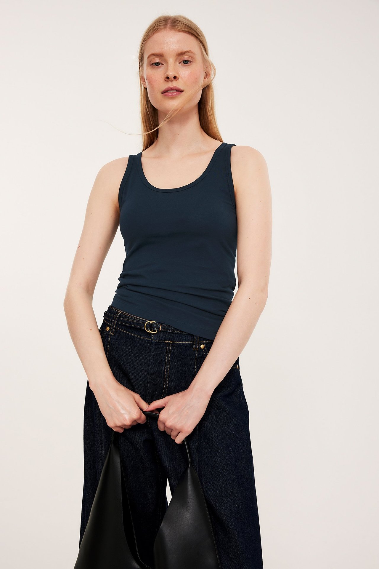 Forfra: kvinne i mørkeblå stretchtopp, mørkeblå vide jeans, holder en svart håndveske.