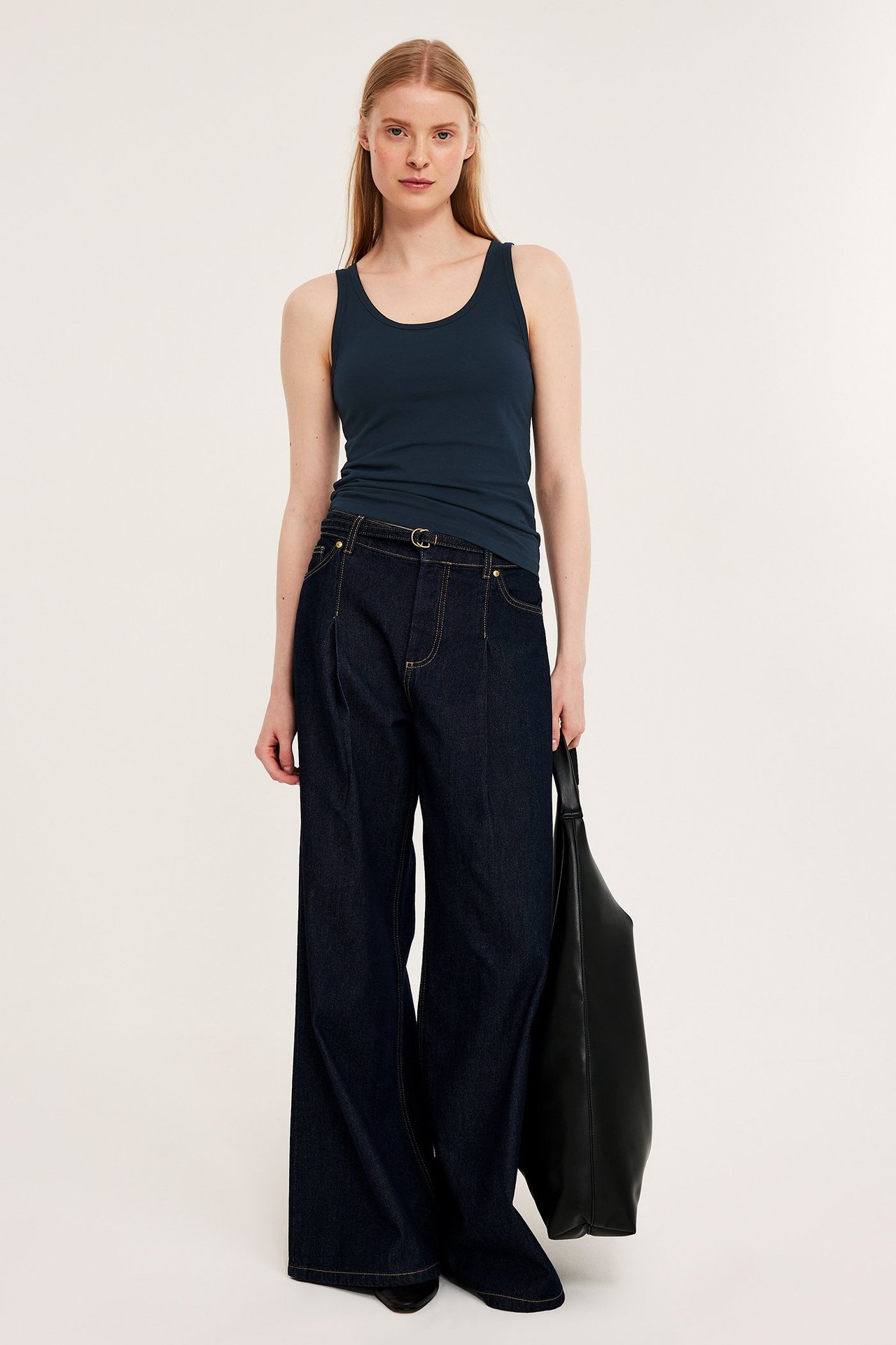 Frontvisning: kvinne i mørkeblå figurnær singlet, mørkeblå vide jeans og en svart håndveske.
