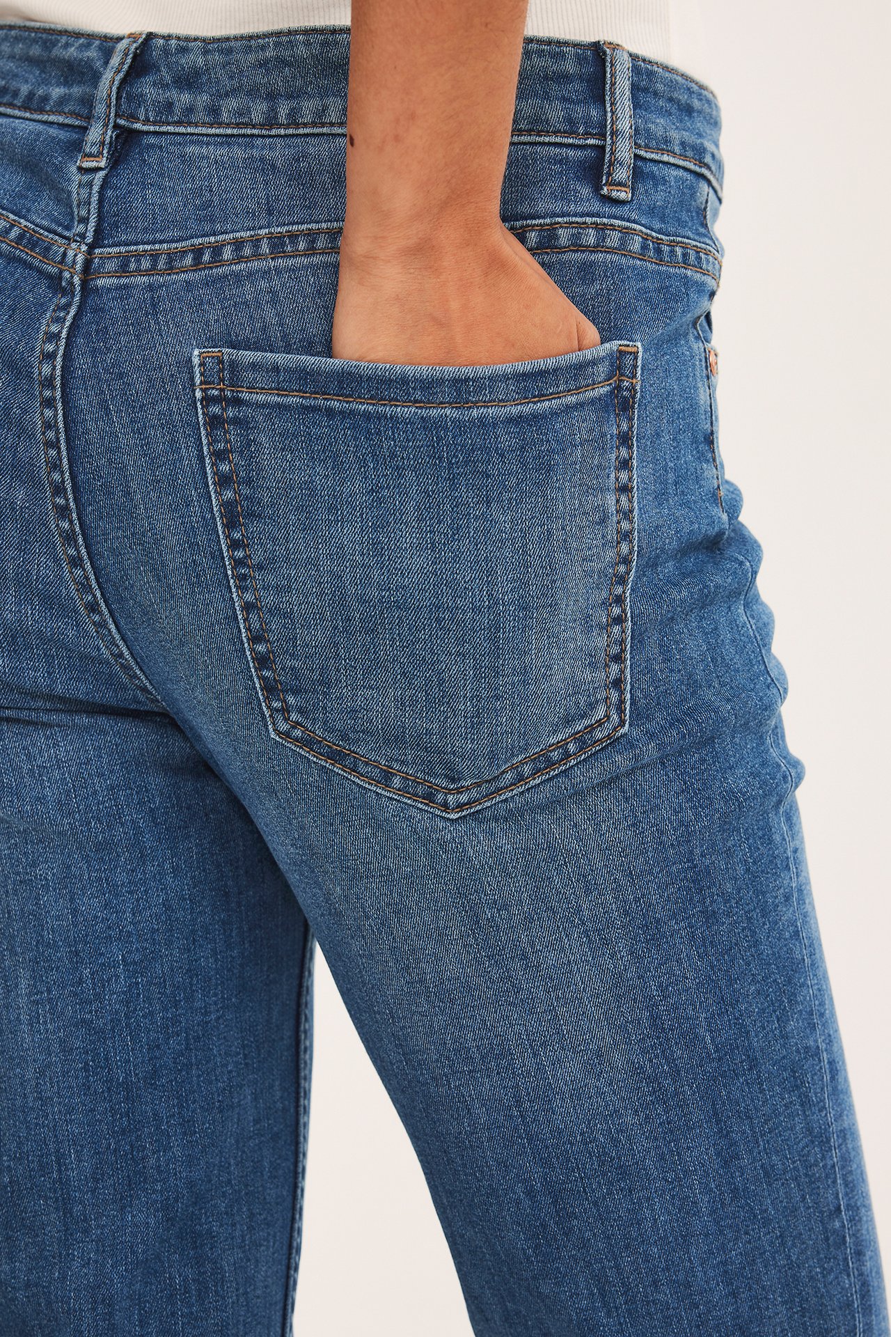 Lähikuva takaa naisen kädestä sinisten denim suorien farkkujen takataskussa.