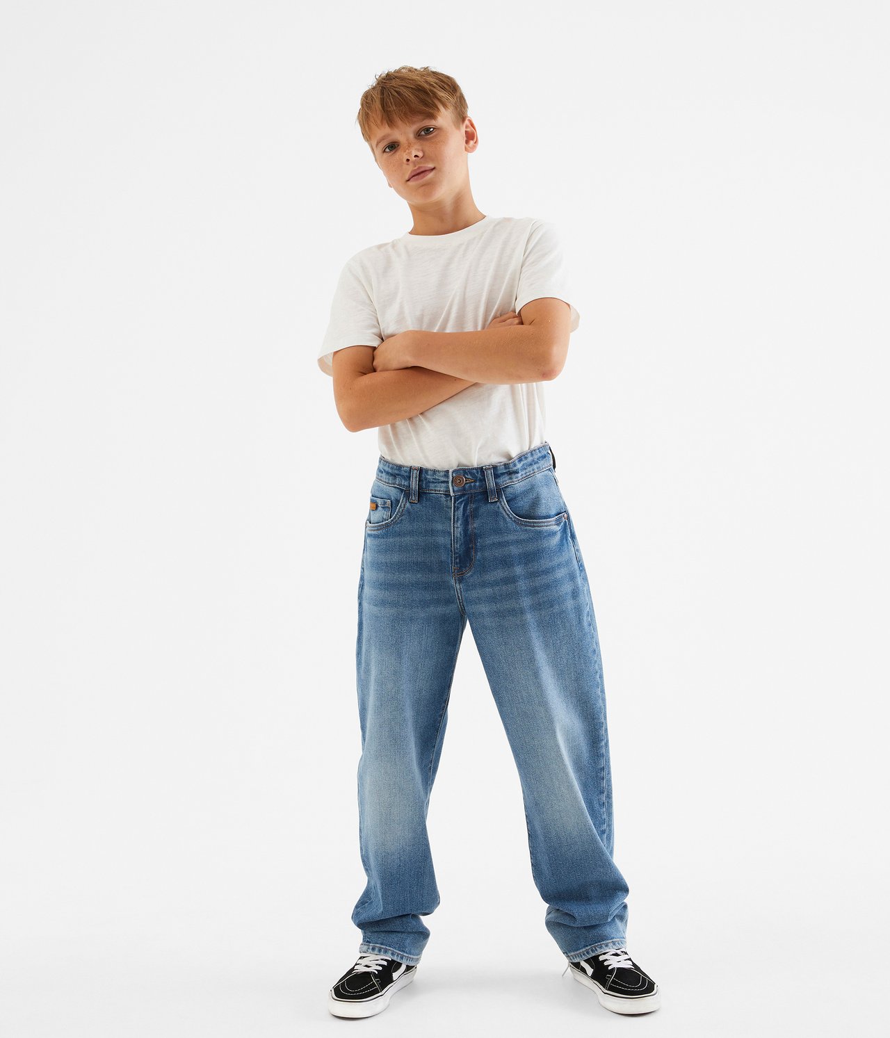 Edestäpäin, lapsi yllään siniset denim baggy loose fit farkut, valkoinen t-paita ja mustat tennarit.