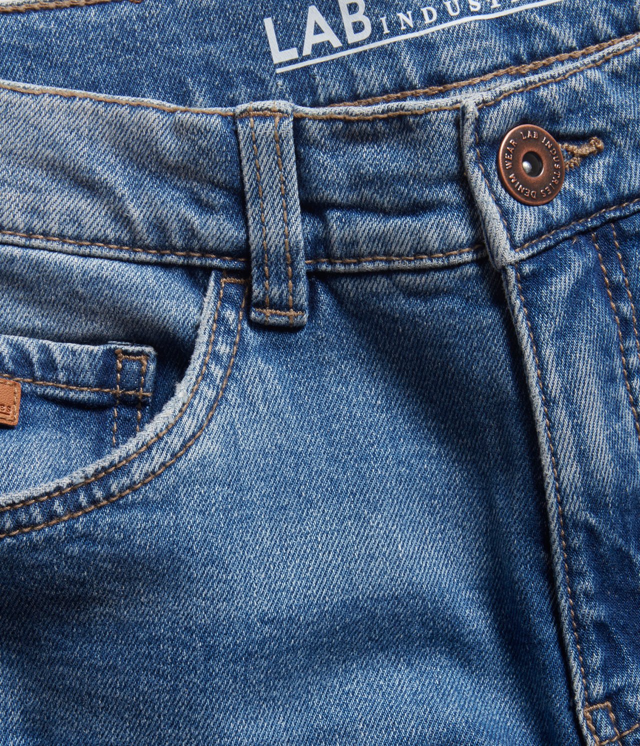 Lähikuva edestä sinisistä denim-baggy-farkuista, joissa kuparinvärinen nappi ja etutasku.