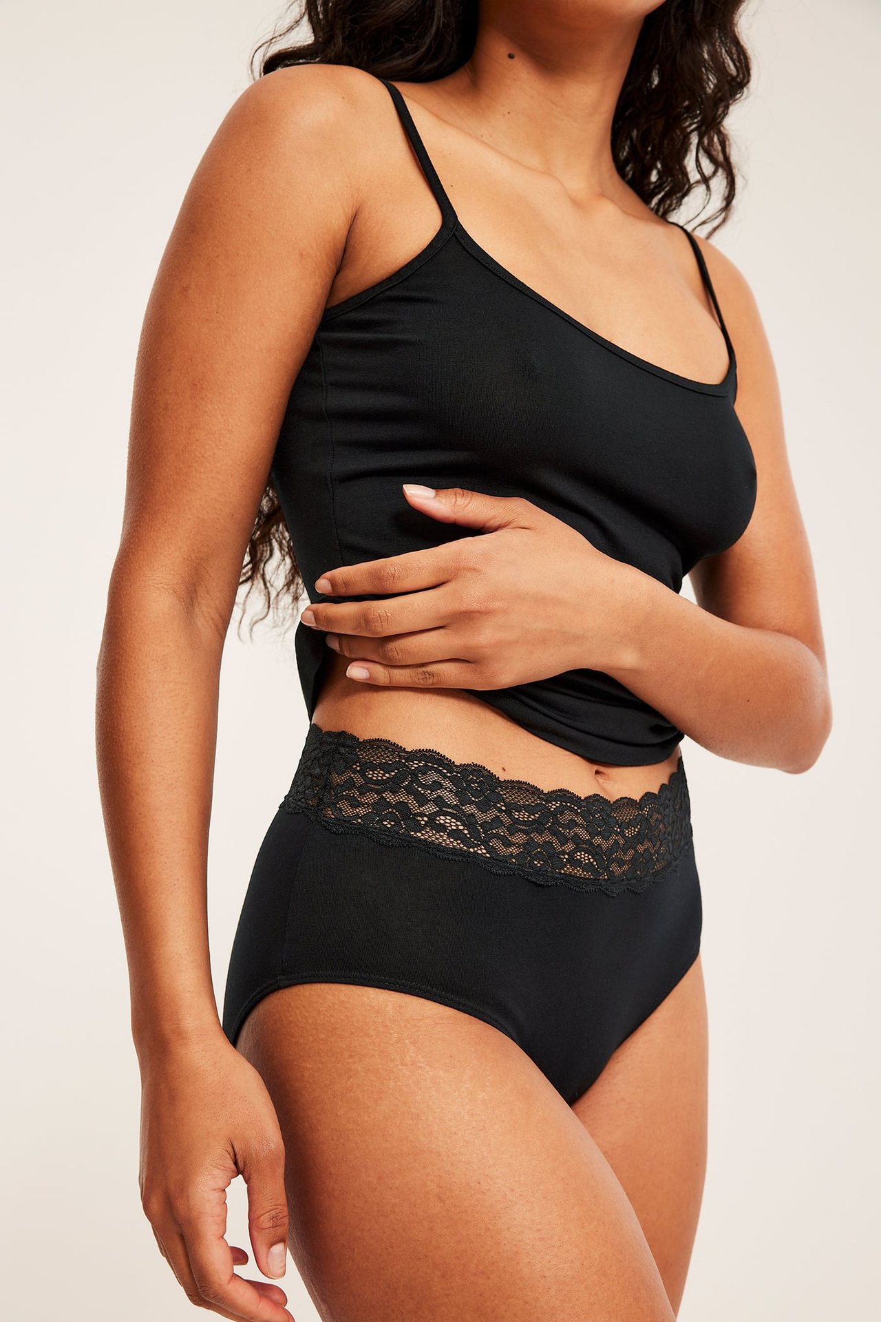 Front av kvinne som har svarte høy-midje truser med blonder og en svart singlet.