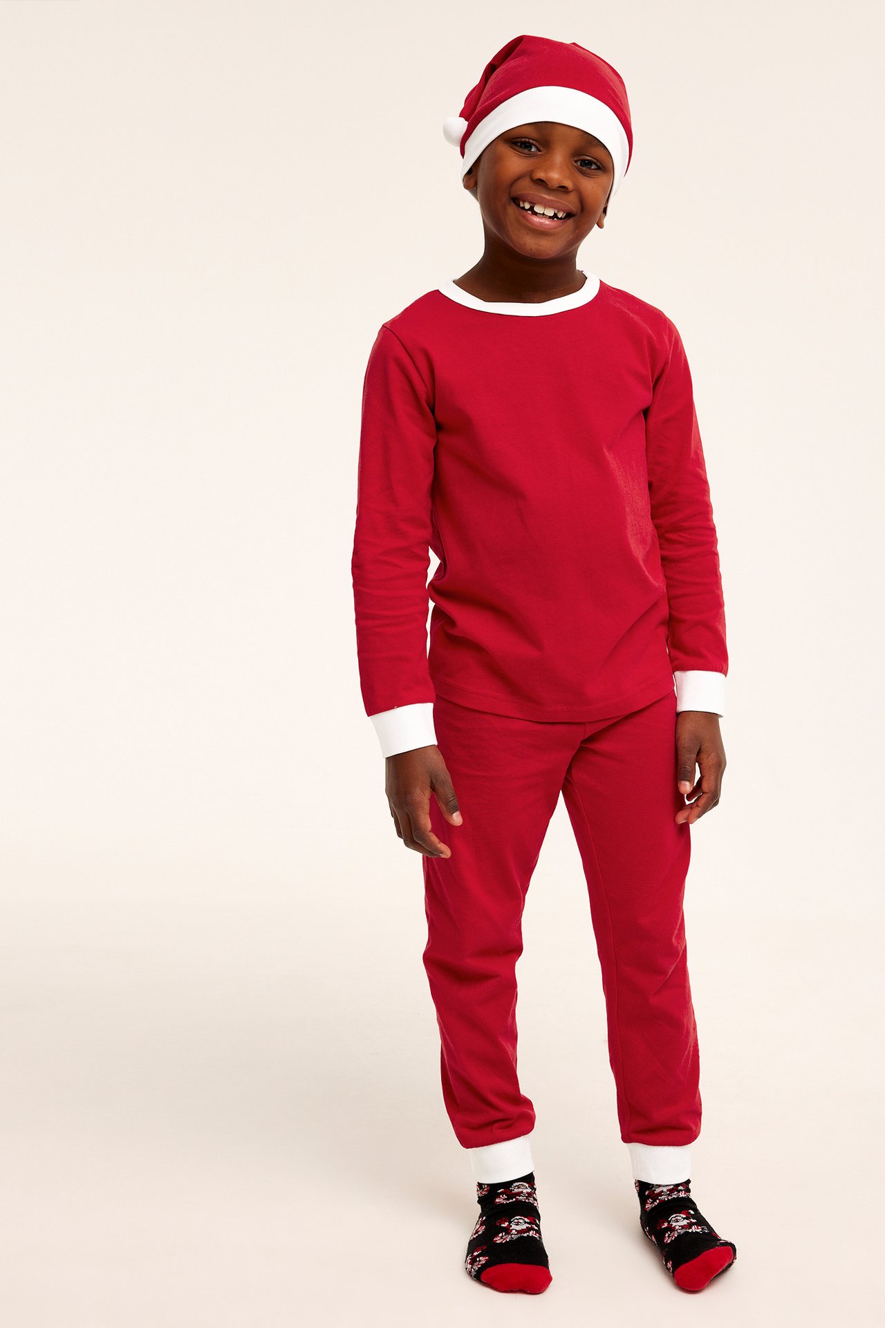 Framifrån: Kid i röd tomtedräkt med vit kant, matchande mössa och mönstrade julsockor.