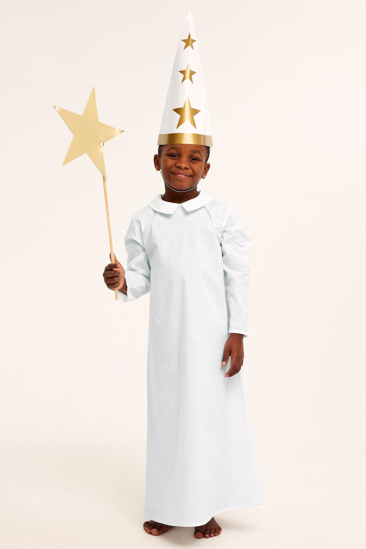 Dziecko w białym nightgown z tylnymi guziczkami, trzyma gwiazdkę i kapelusz gwiazdy.