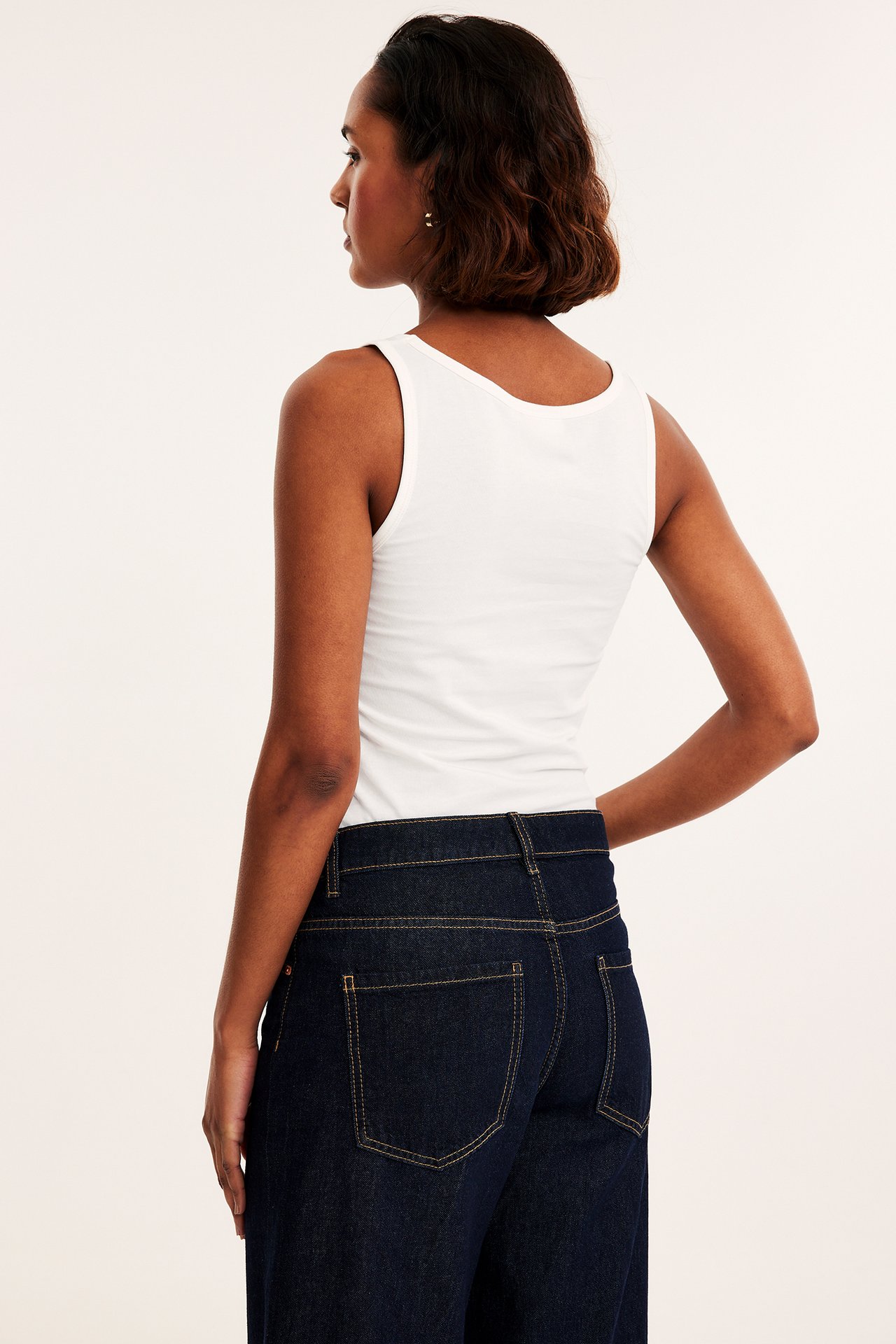 Bakfra, kvinne i en figurnær offwhite stretchtopp og mørkeblå jeans.