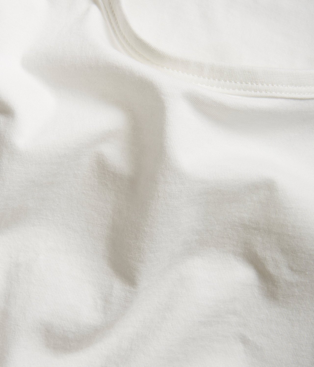 Nærbilde av en offwhite basistopp, som viser det myke, elastiske bomull-elastan-stoffet med synlige sømmer.