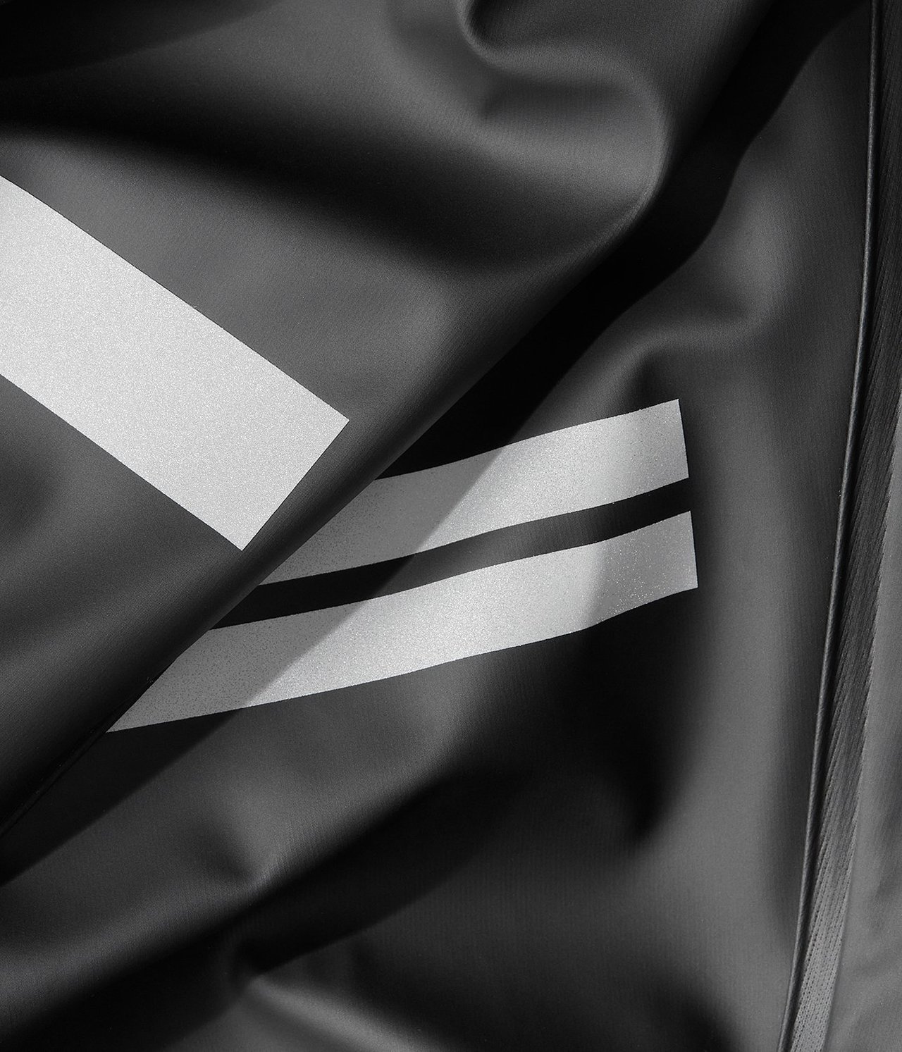 Zbliżenie na czarne spodnie przeciwdeszczowe z poliestru z odblaskowymi białymi paskami.