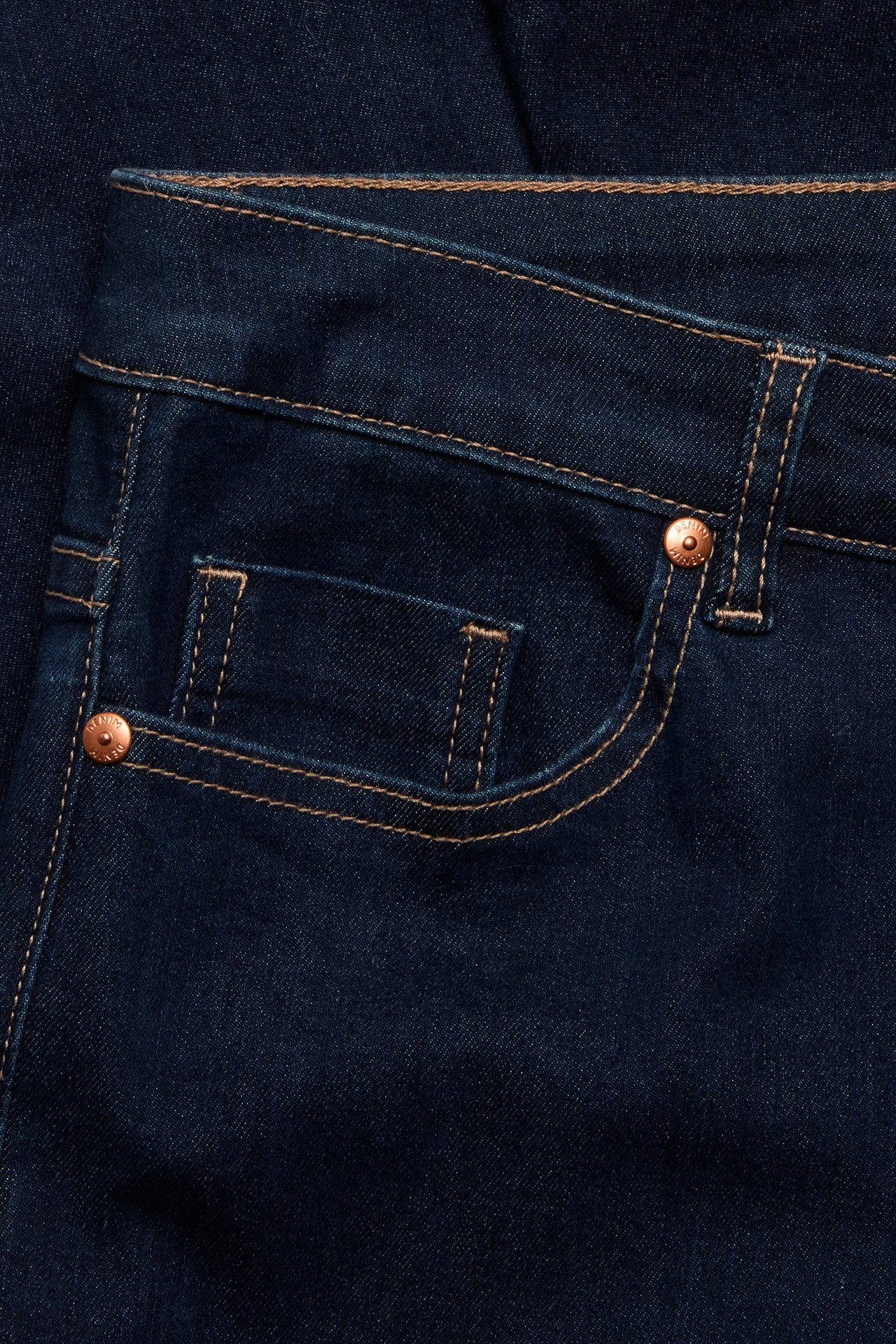 Zbliżenie na ciemnoniebieskie proste jeansy, przednia kieszeń z jasnymi szwami i miedzianymi nitami.