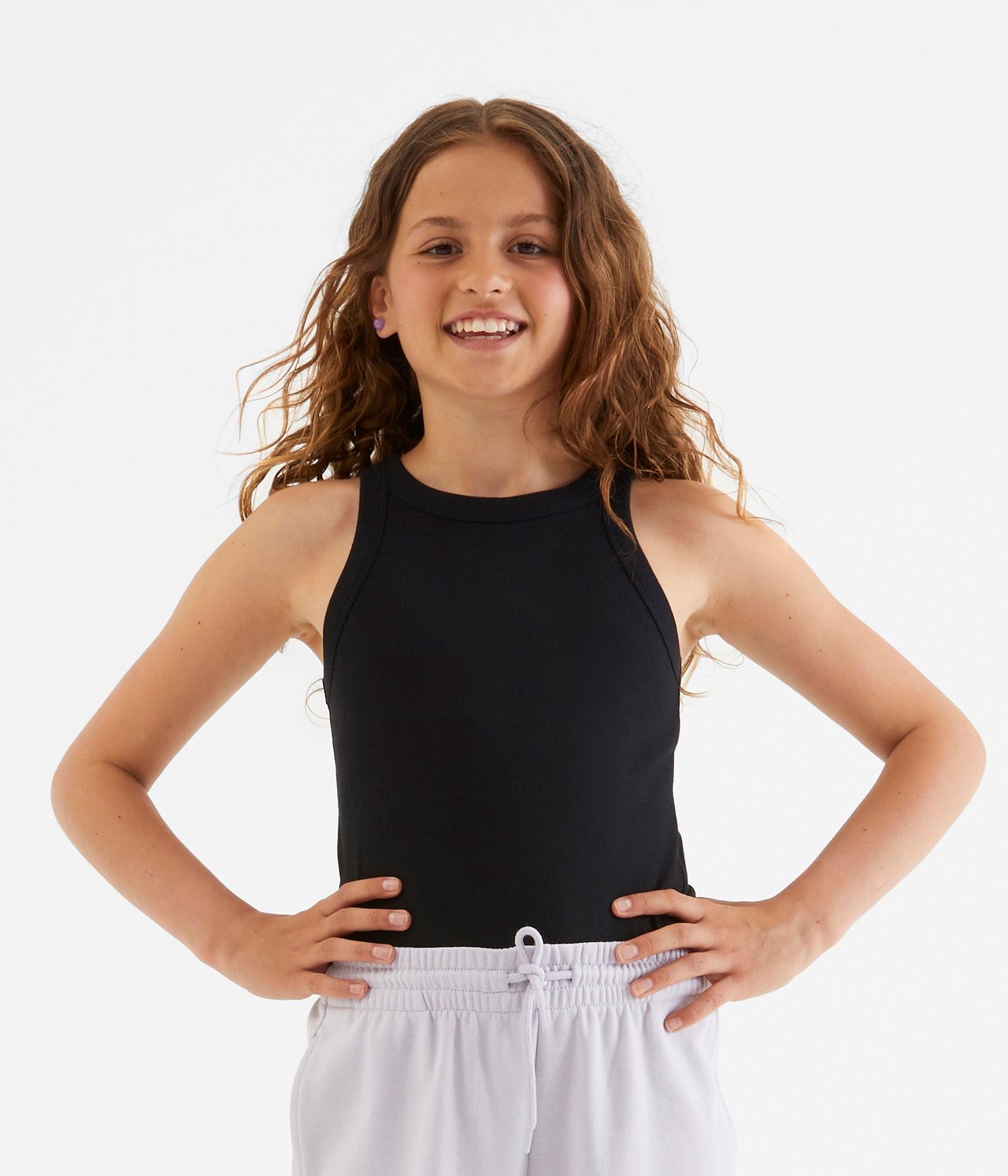 Frontvy av ett barn i ett svart ribbat linne och ljuslila mjukisbyxor.