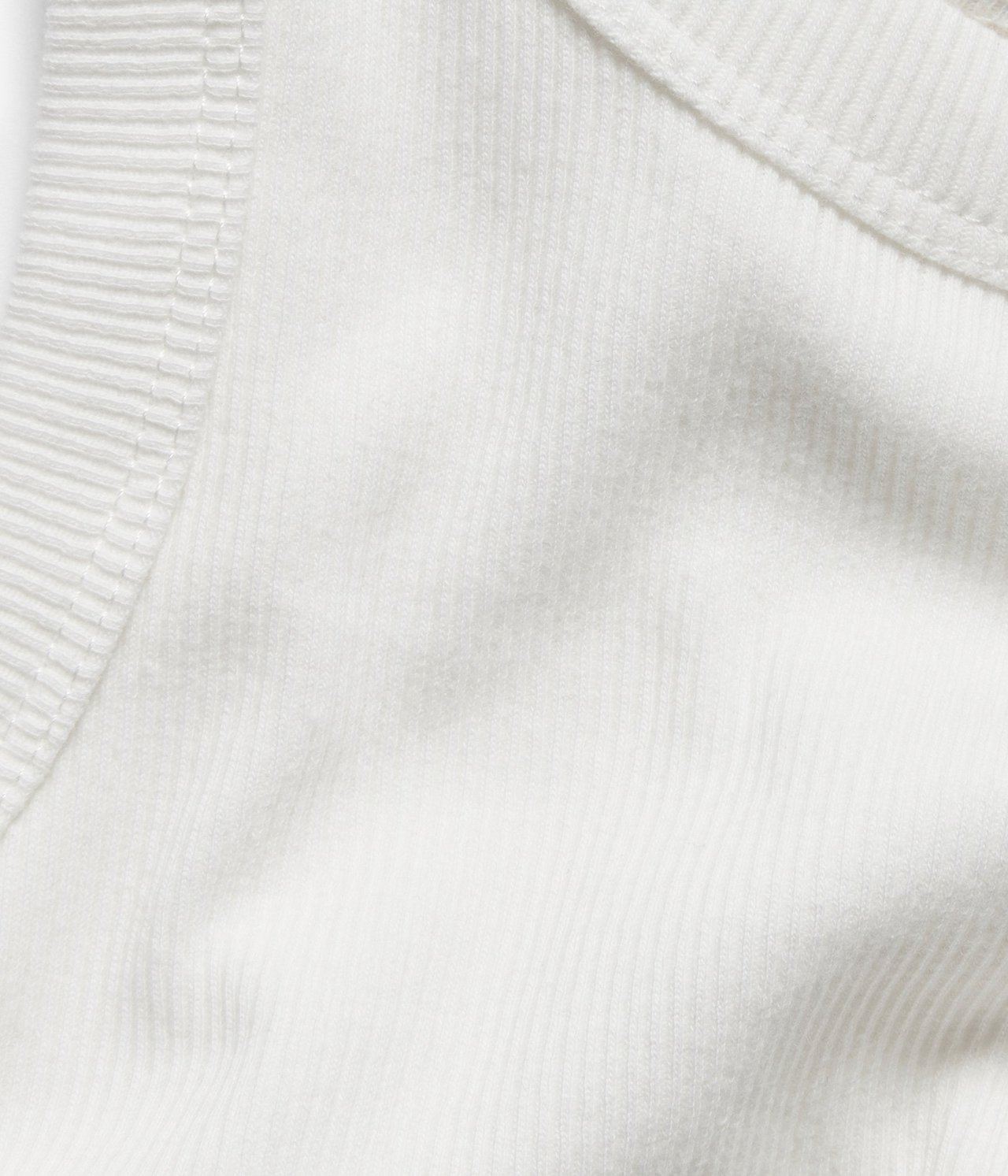 Zbliżenie na tkaninę kremowego, prążkowanego topu, ukazujące teksturowany splot.