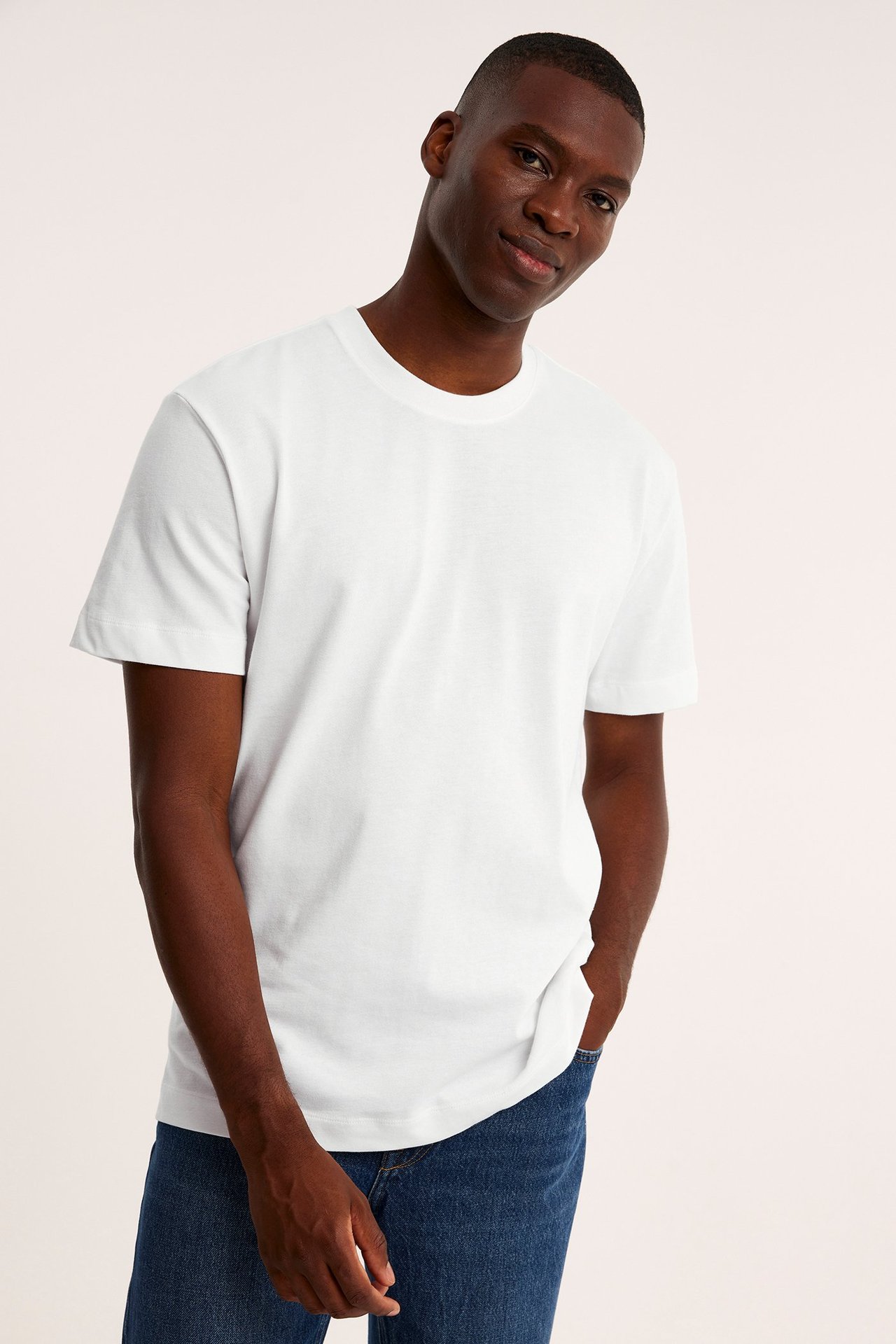 Frontbilde av mann i off-white løstsittende bomulls-t-skjorte og blå jeans, hånd i lommen.
