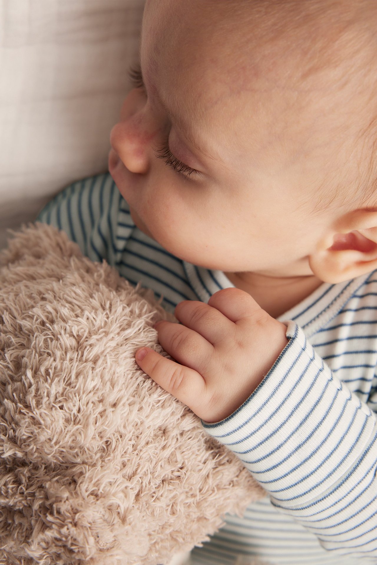 Lähikuva vauvasta sinivalkoraidallisessa pitkähihaisessa bodyassa, pitäen vaaleanruskeaa nallekarhua.